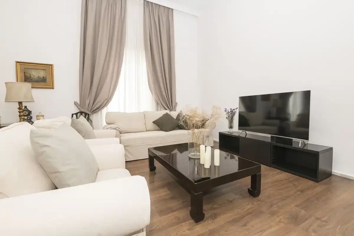 A bright living room with light seating, a coffee table, and a television.