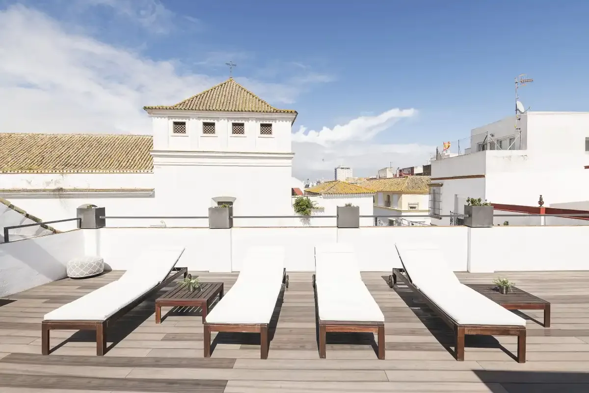 A rooftop terrace with rows of lounge seating and white buildings beyond.