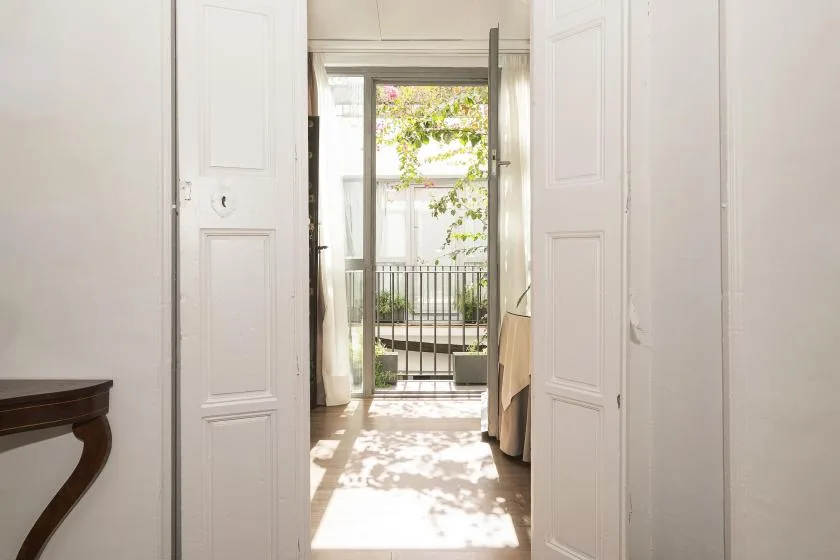 A bright interior passage opens through white doors toward a sunlit balcony.