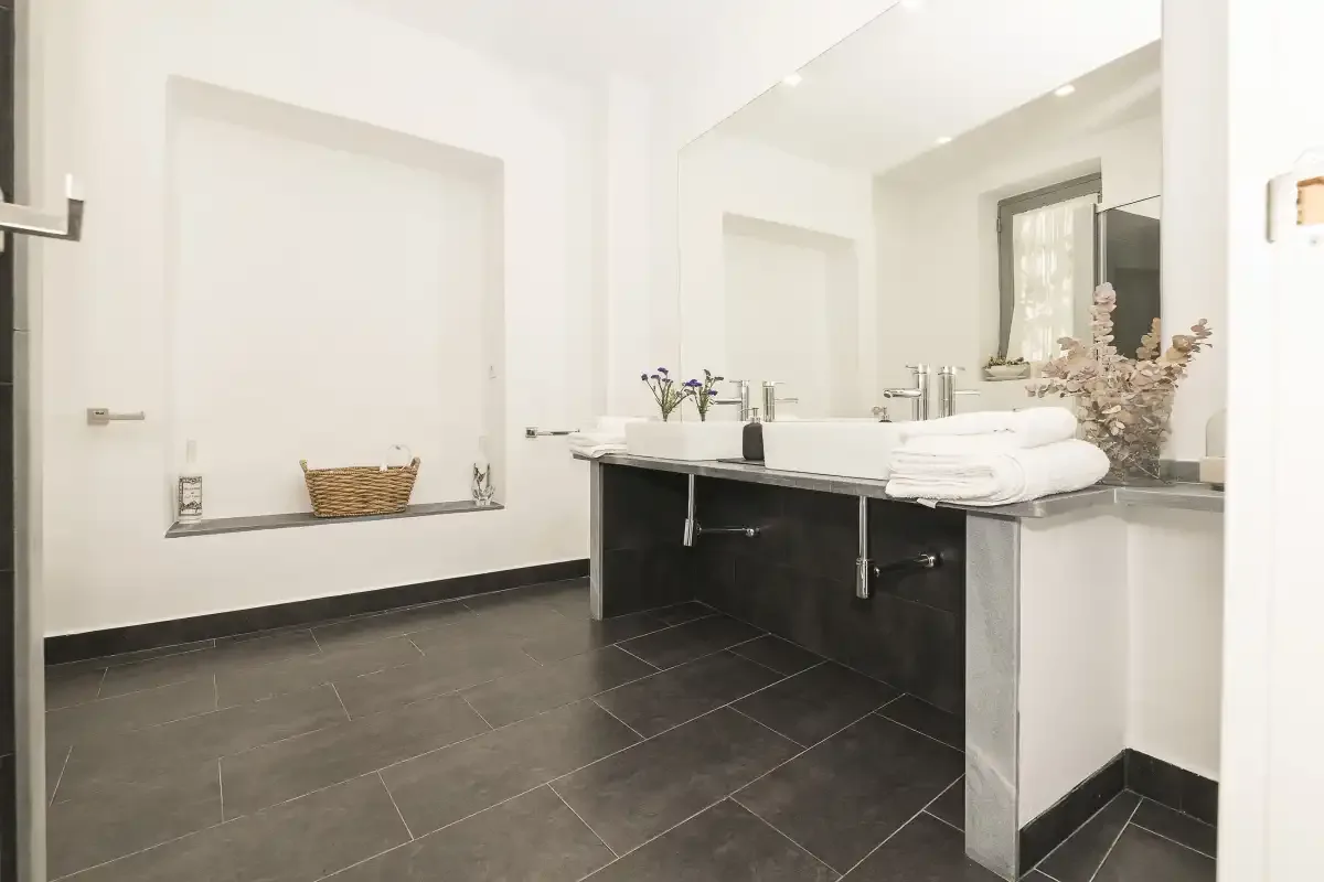 A bright bathroom with a long vanity, wide mirror, and dark floor.