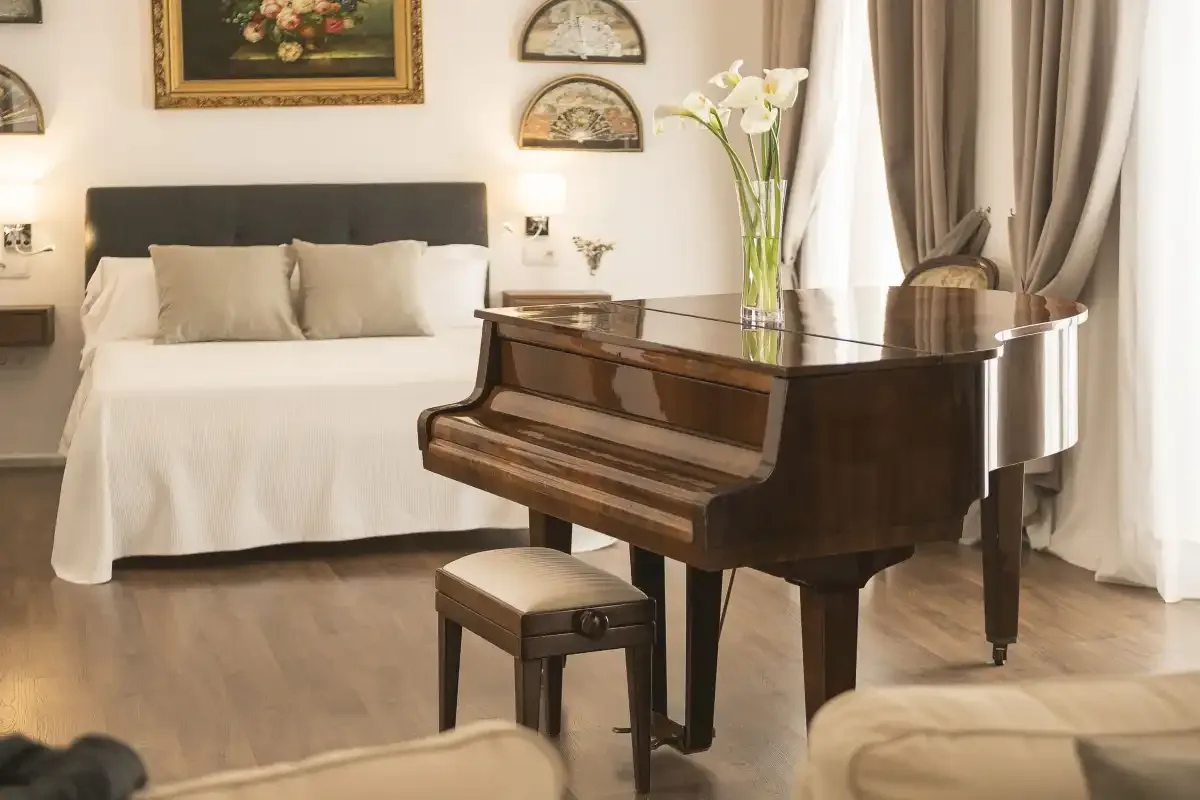 A bedroom with a neatly made bed and a grand piano in the foreground.