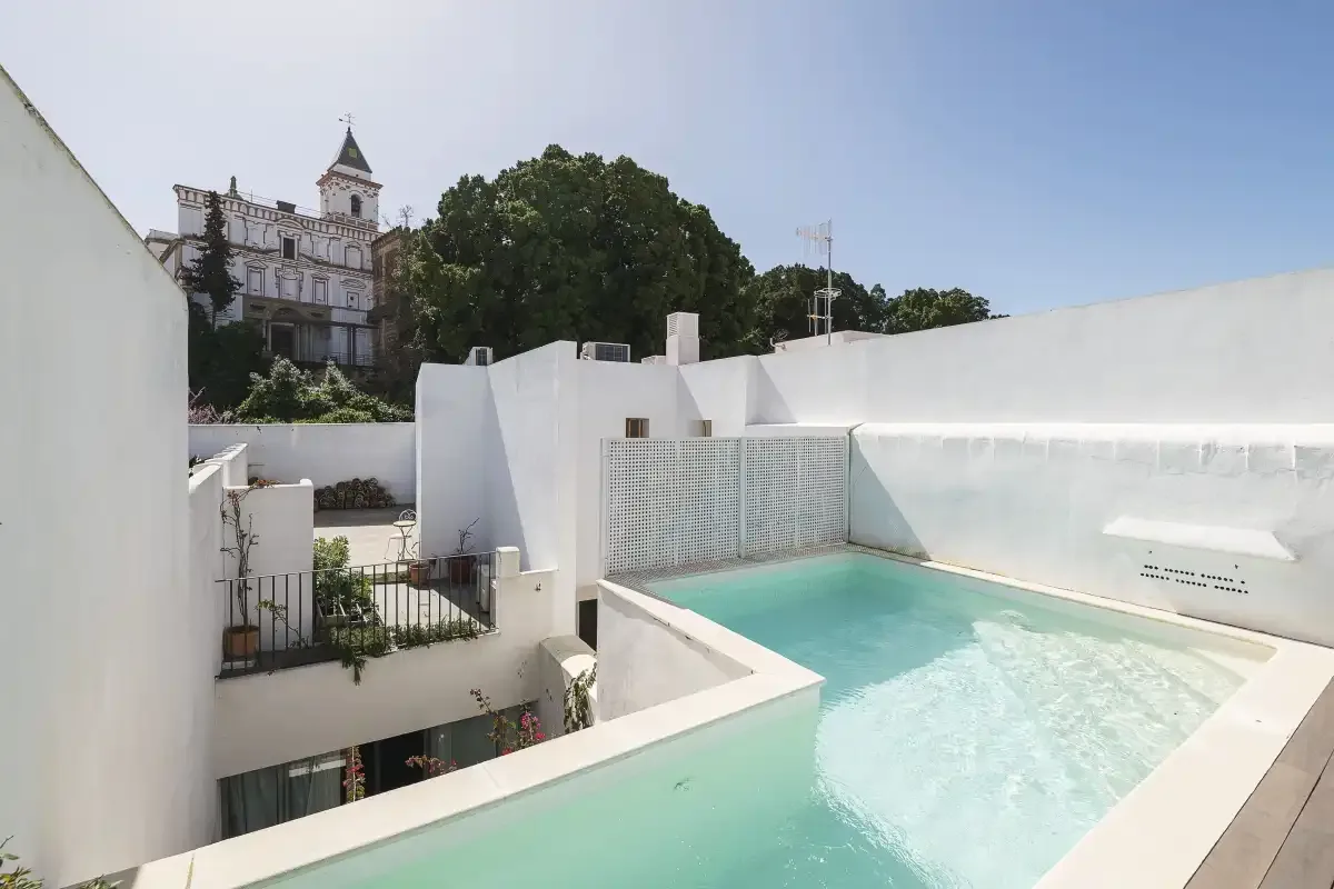 A rooftop pool surrounded by white walls and overlooking nearby buildings.