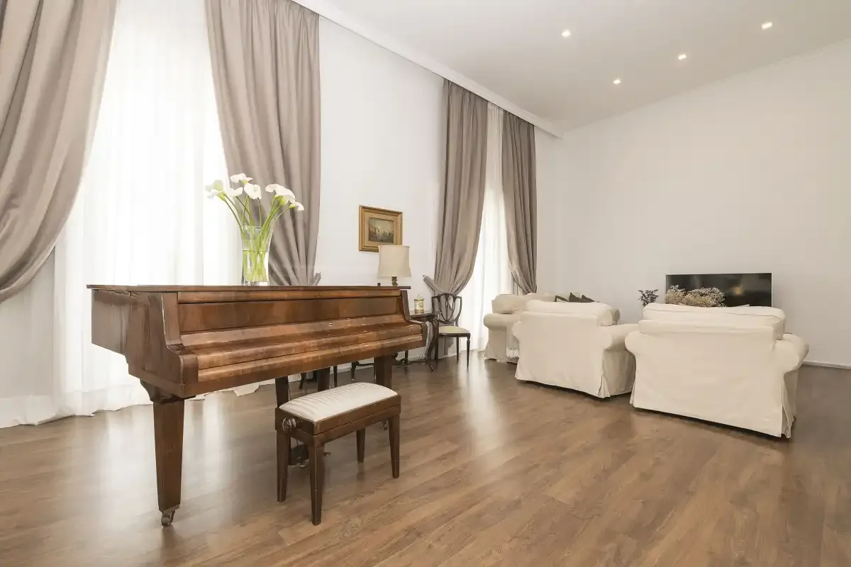 A bright living room with a grand piano, seating, and tall curtained windows.