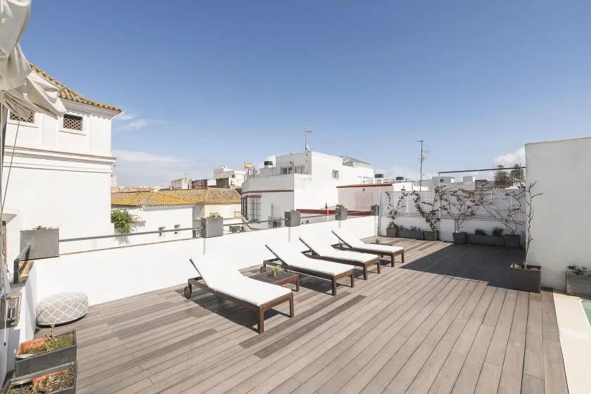 A sunny rooftop terrace with lounge seating and potted plants.