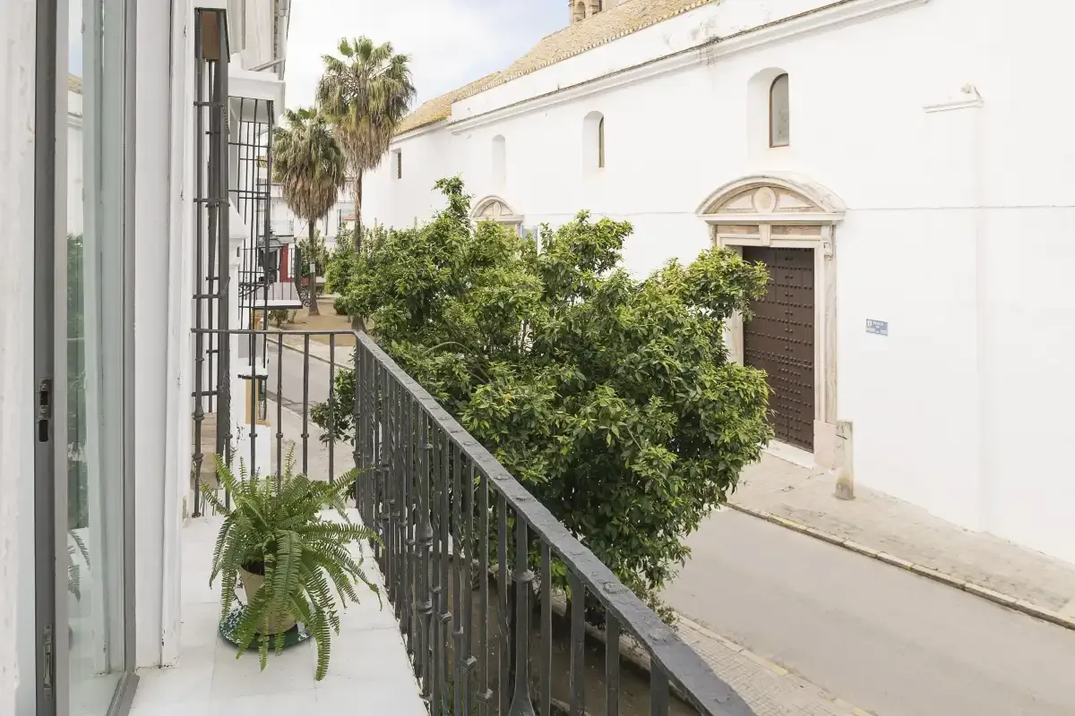 A balcony overlooks a leafy courtyard and a white building.