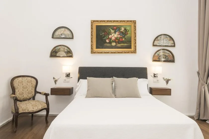 A bedroom with a neatly made bed, wall art, and an upholstered chair.