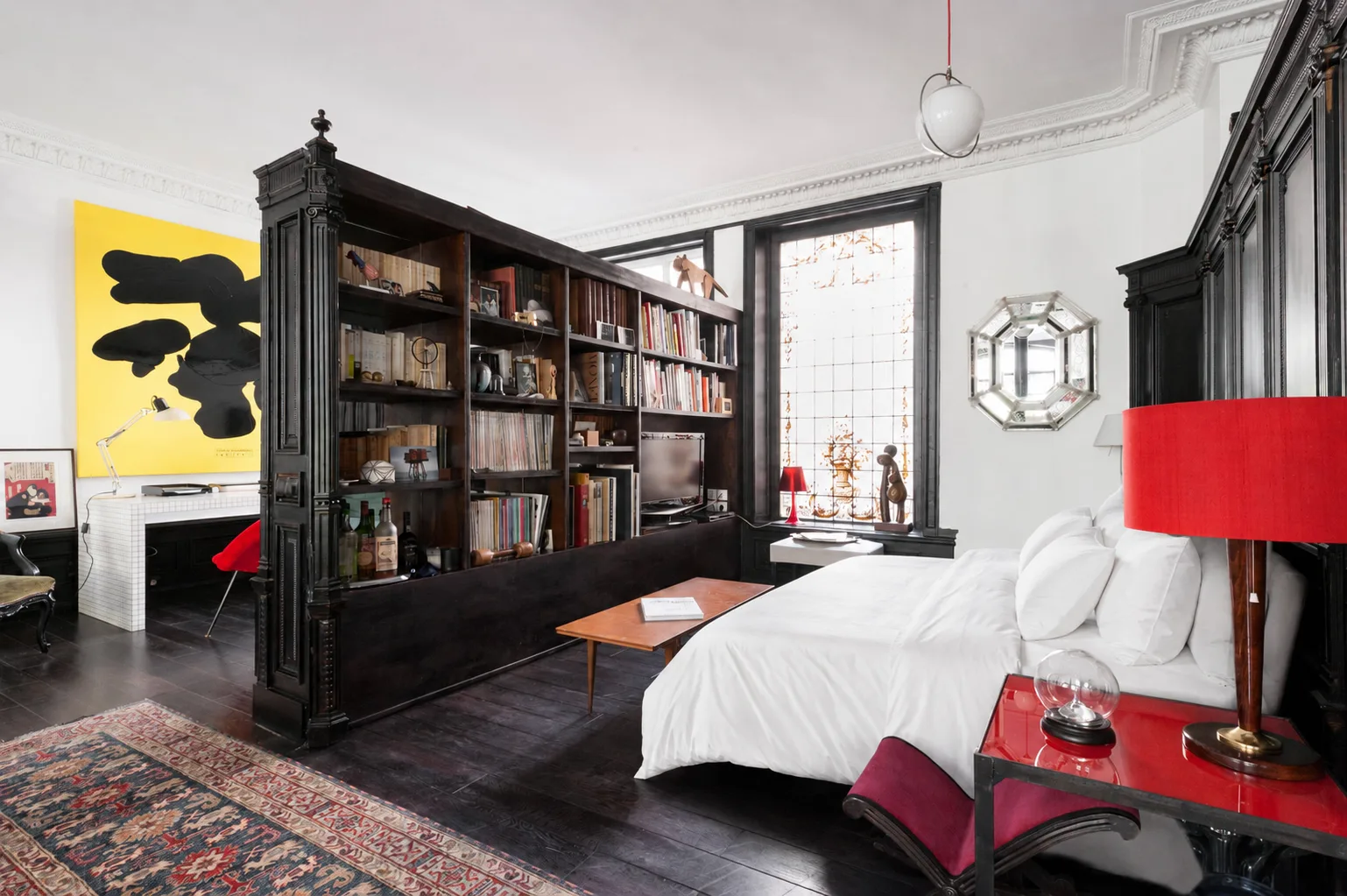 A bedroom with a white bed, dark bookcases, and a red bedside table.