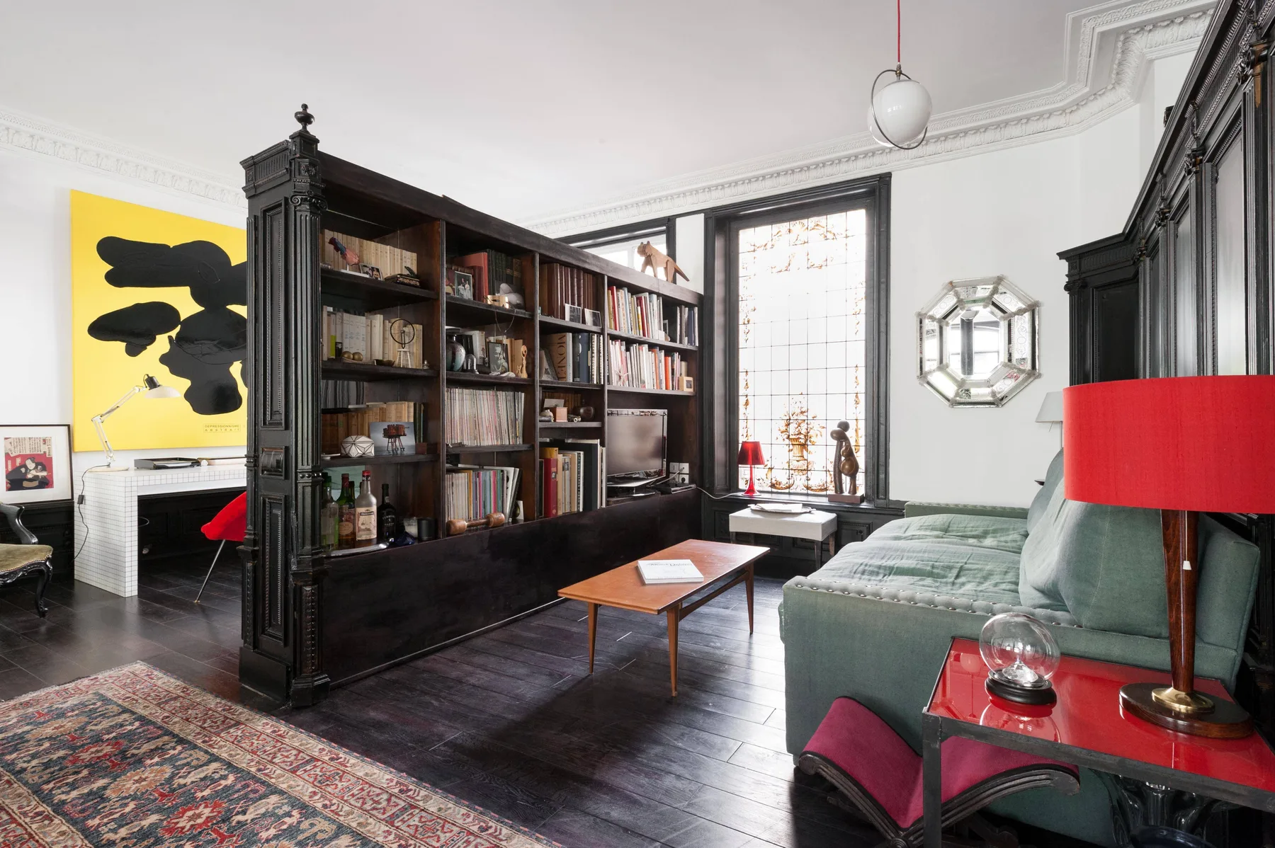 A living room with a large bookcase and seating beside a tall window.