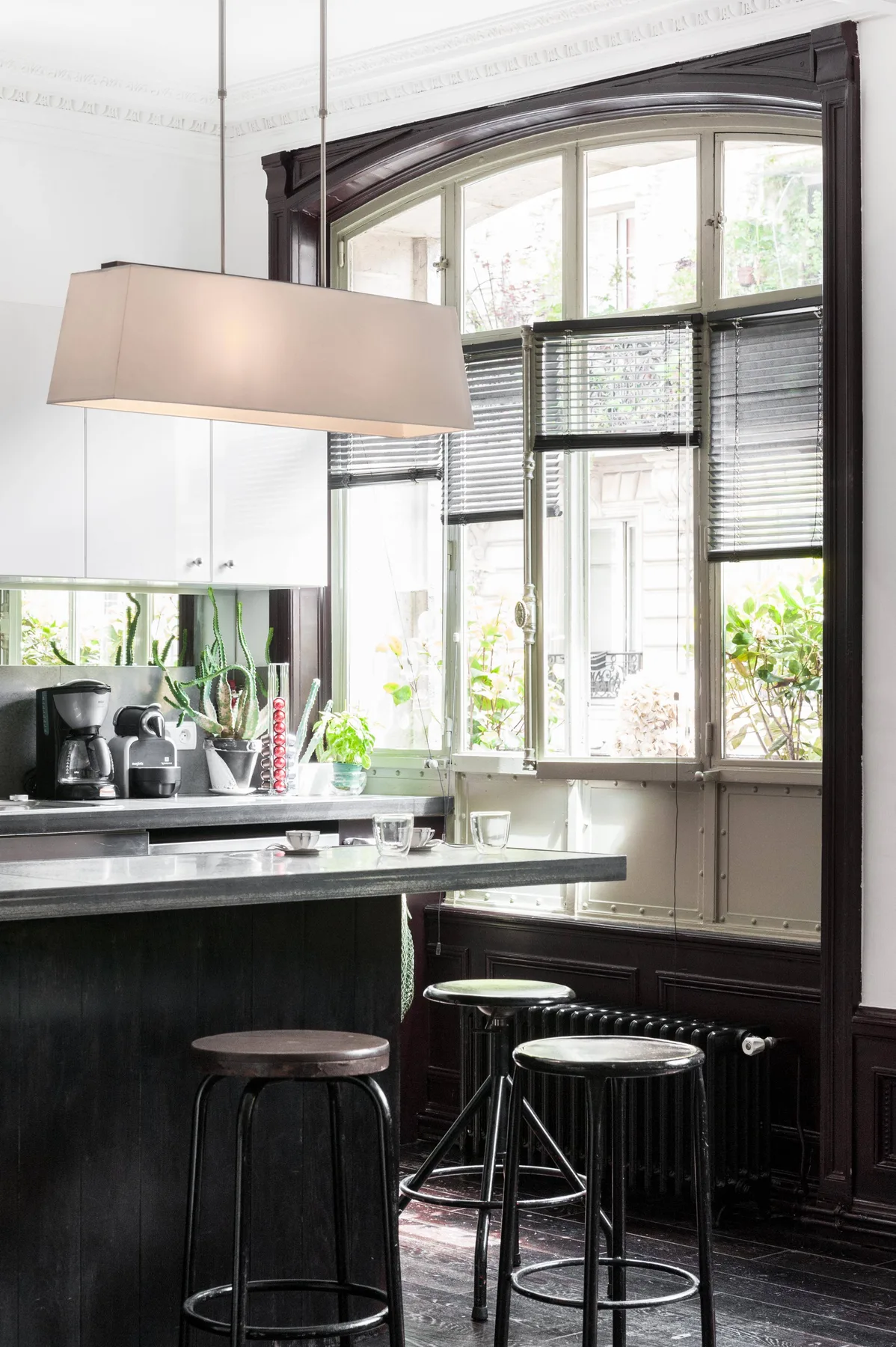 A bright kitchen with a dark counter, stools, and tall windows.