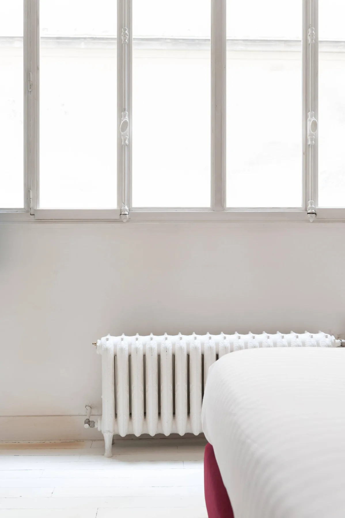 A bright bedroom with a bed beside a radiator and tall windows.