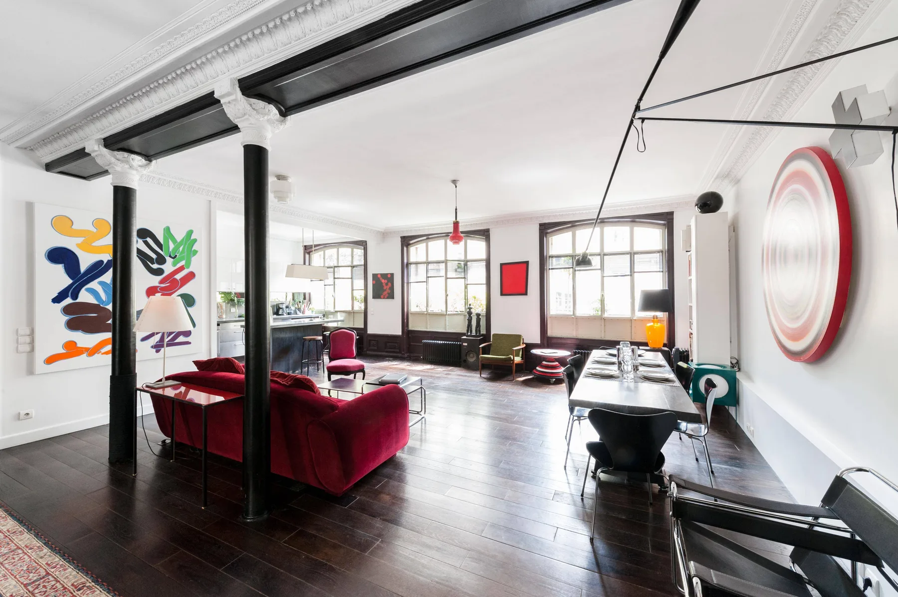 A spacious living and dining room with colorful wall art and dark wood flooring.
