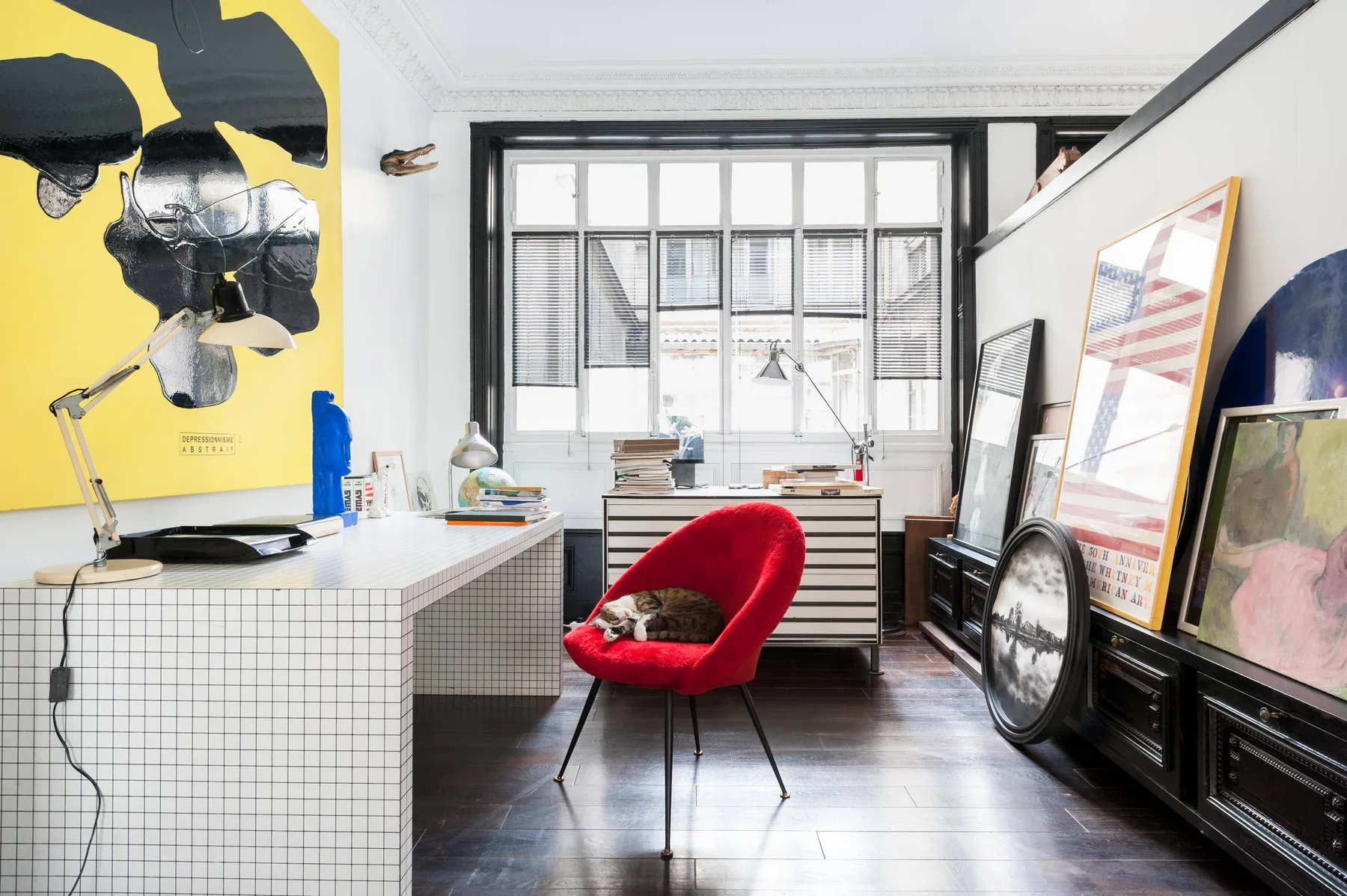 A bright studio workspace with a red lounge chair and large windows.