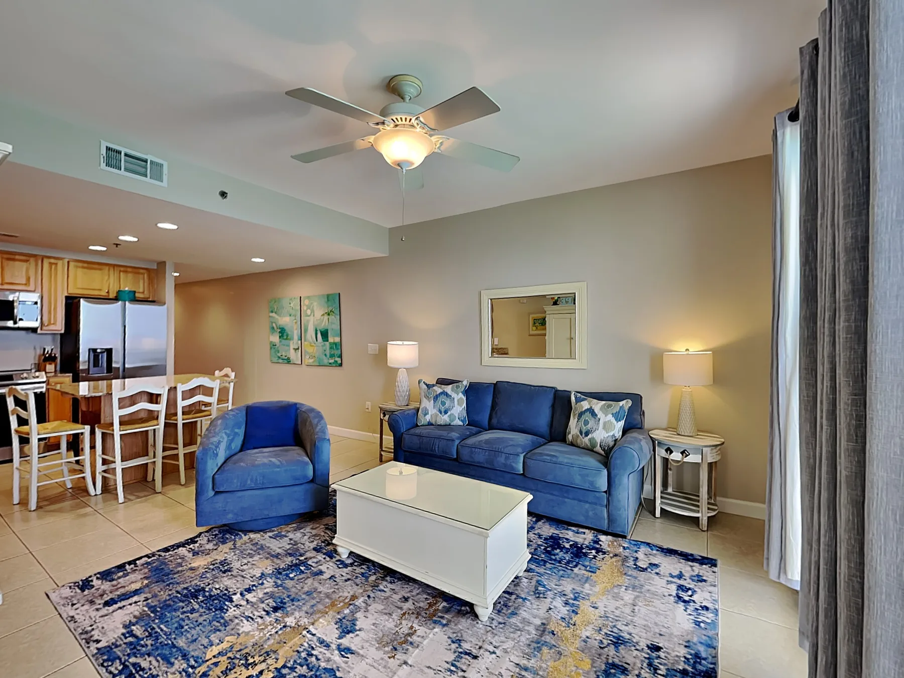 A living room with blue seating, a white coffee table, and an open kitchen.