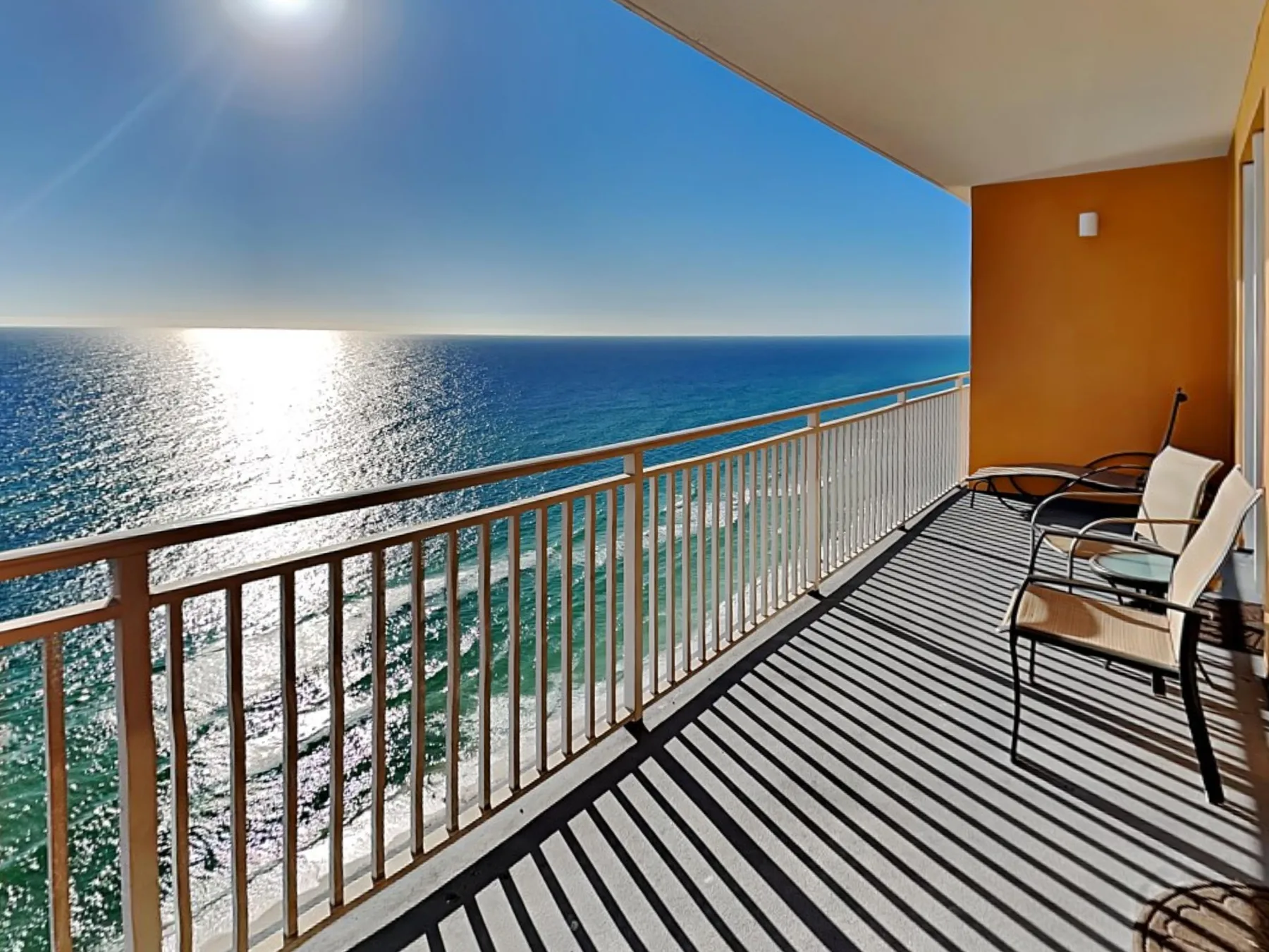 A balcony overlooks the ocean, with outdoor seating beside the railing.
