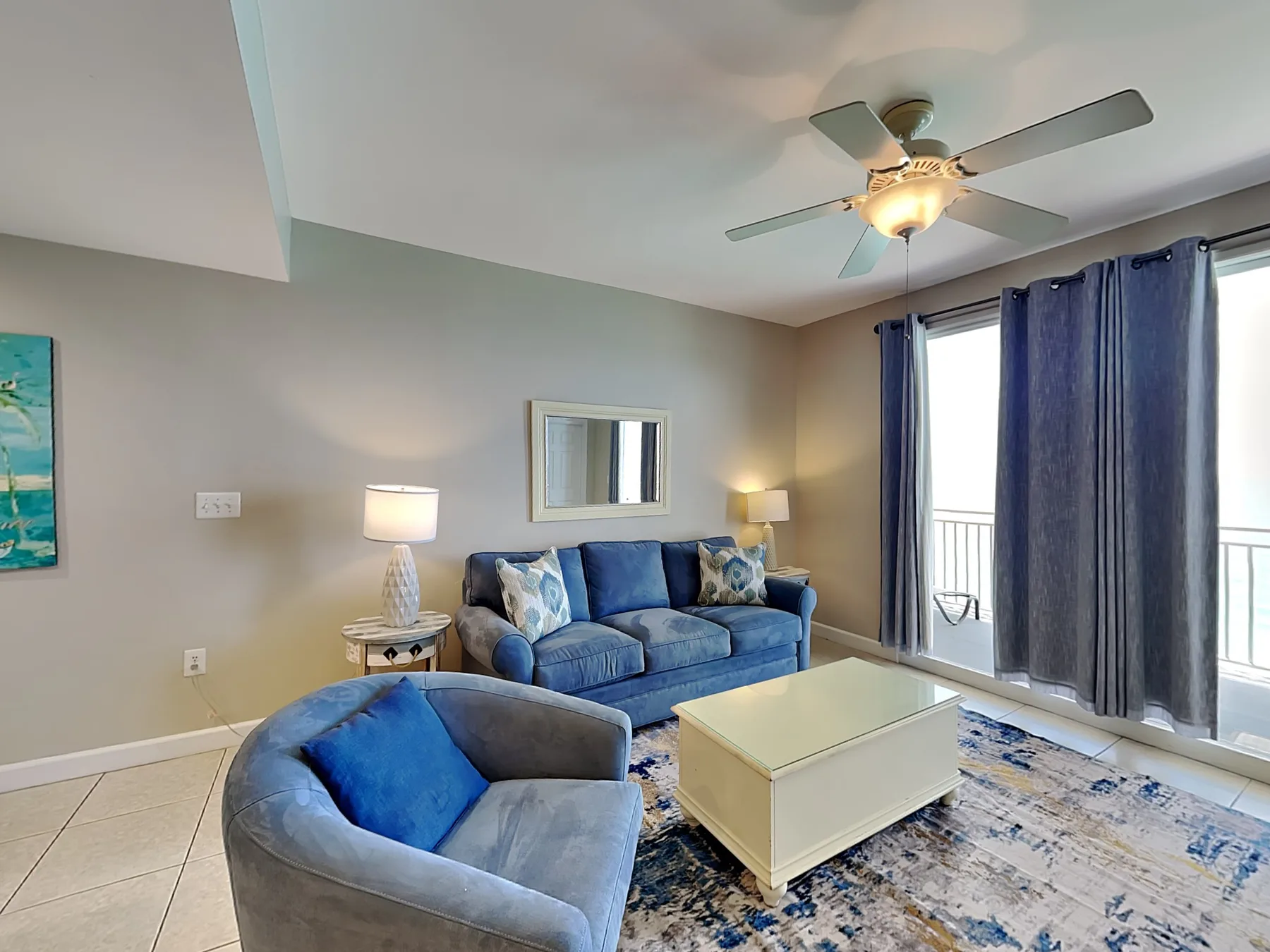 A living room with blue seating, a coffee table, and curtains by the glass doors.