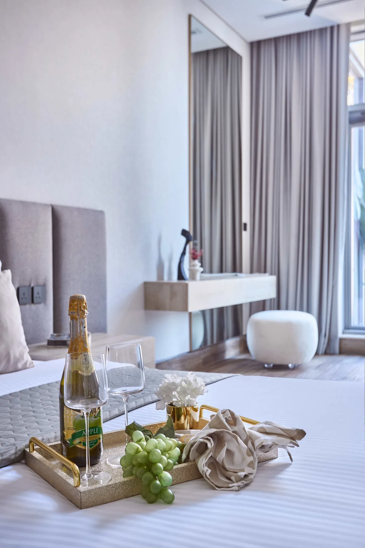 A bedroom with a tray of refreshments on the bed and a vanity by the curtains.