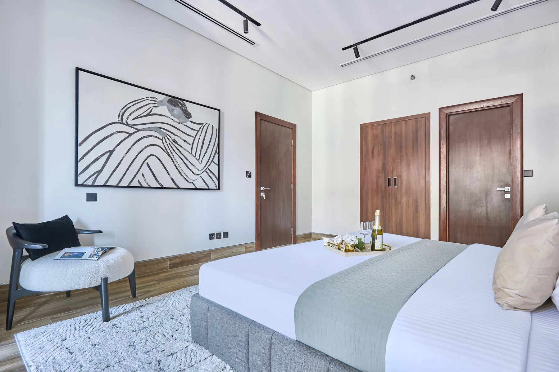 A bright bedroom with a neatly made bed and framed abstract artwork on the wall.