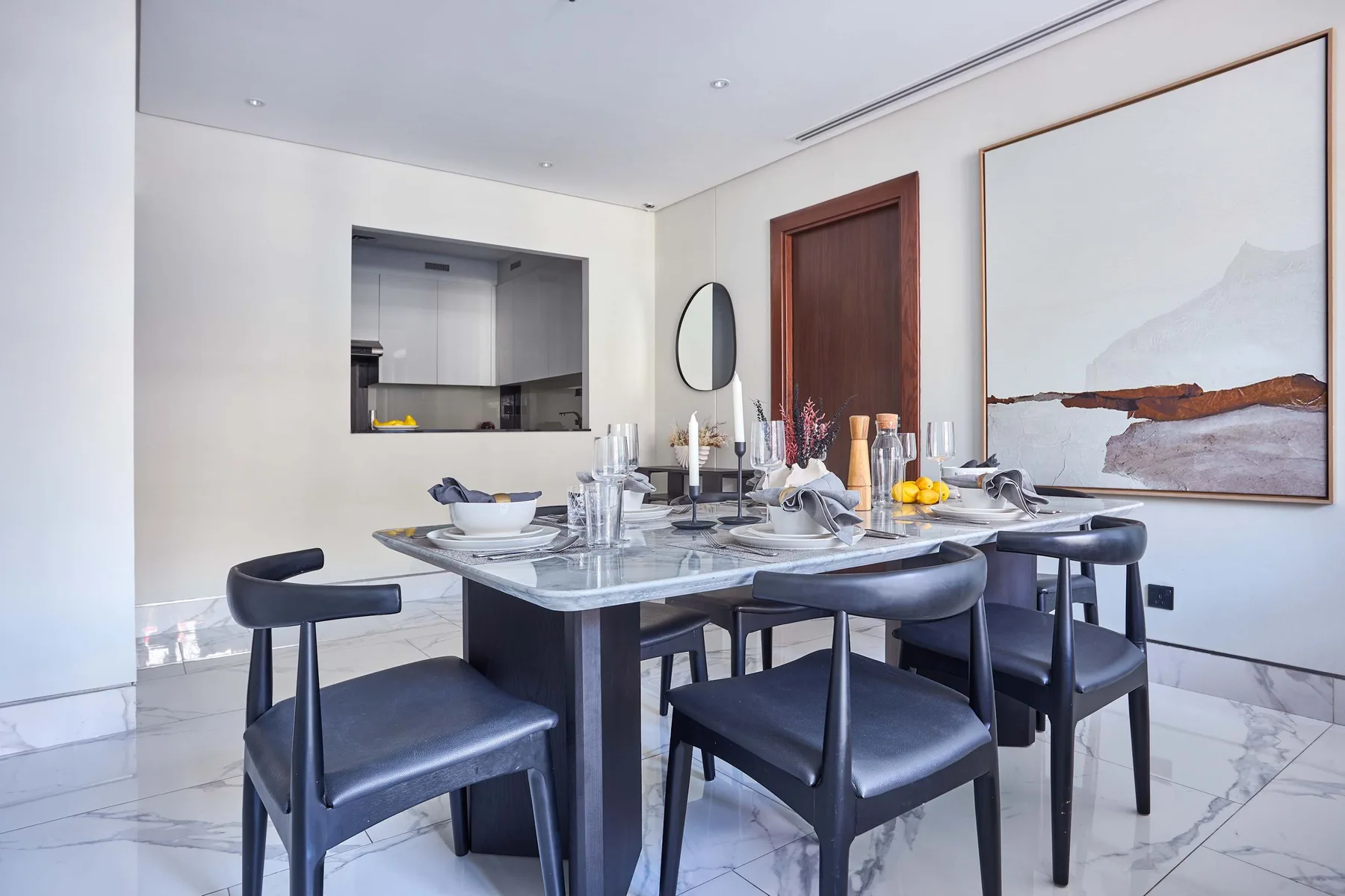 Un comedor con la mesa puesta, asientos oscuros y una obra enmarcada grande.