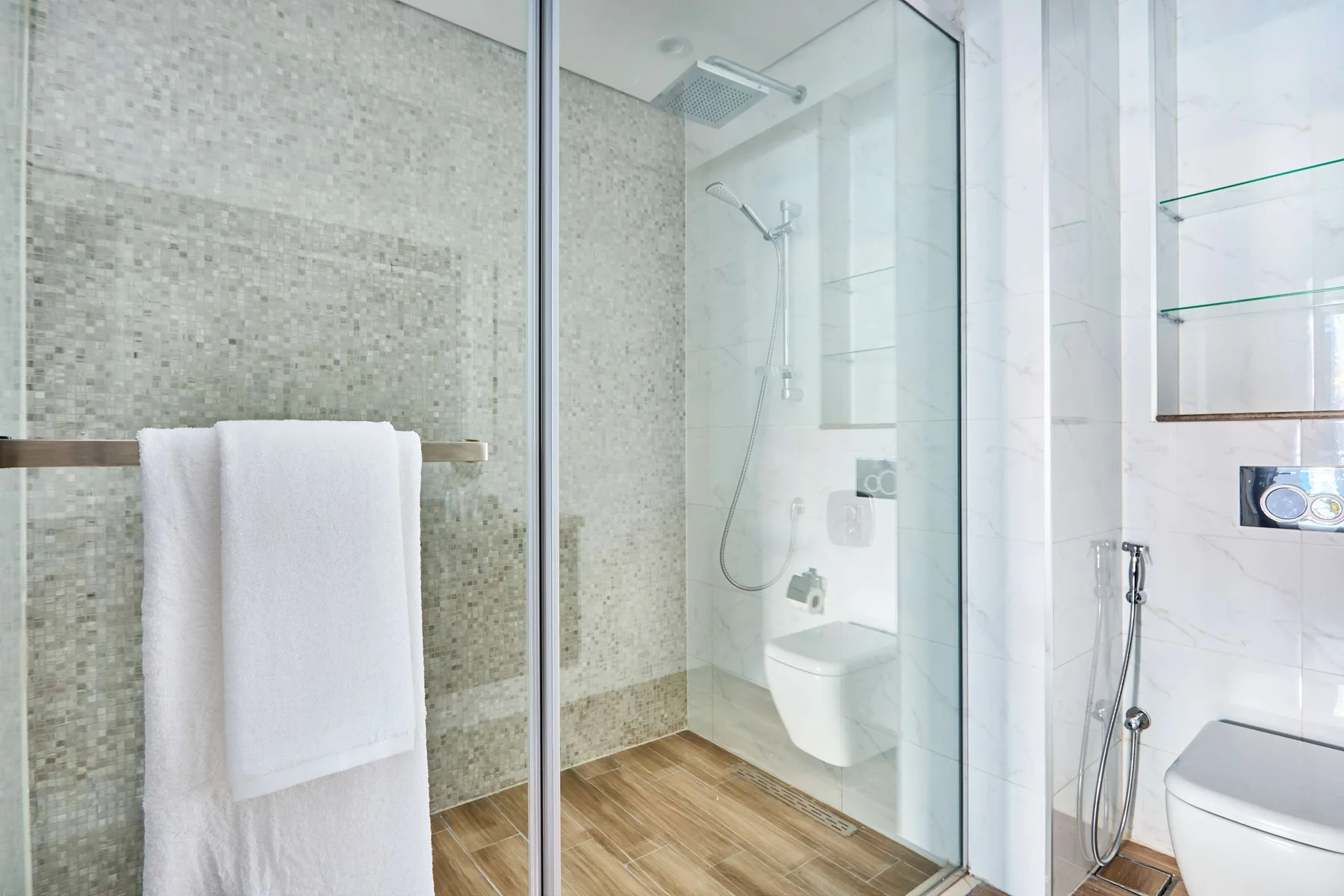 A bright bathroom with a glass shower and a towel hanging nearby.