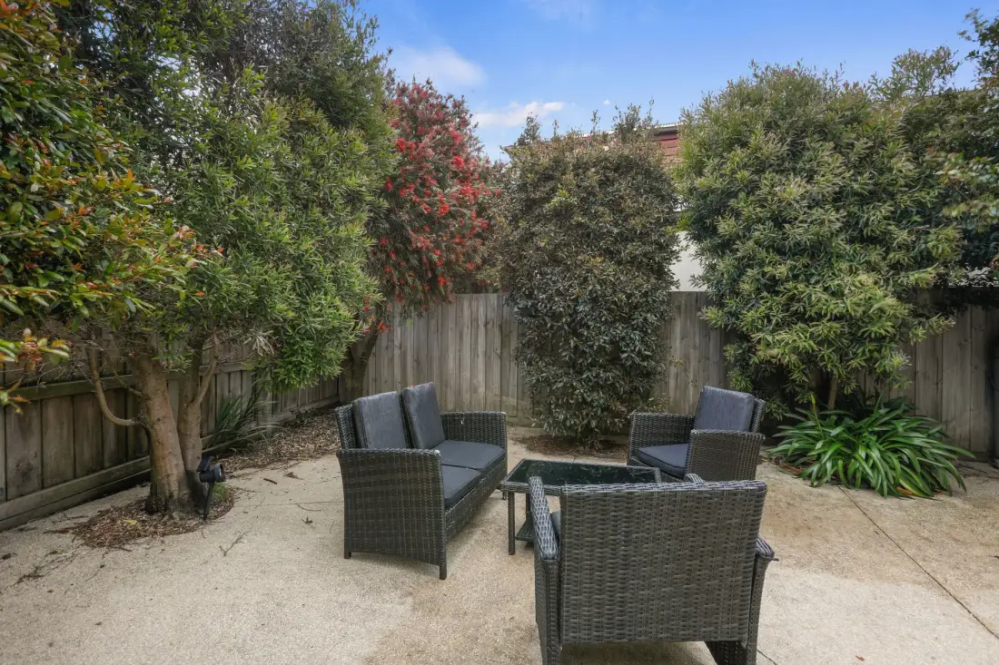 A garden patio with outdoor seating surrounded by shrubs and trees.