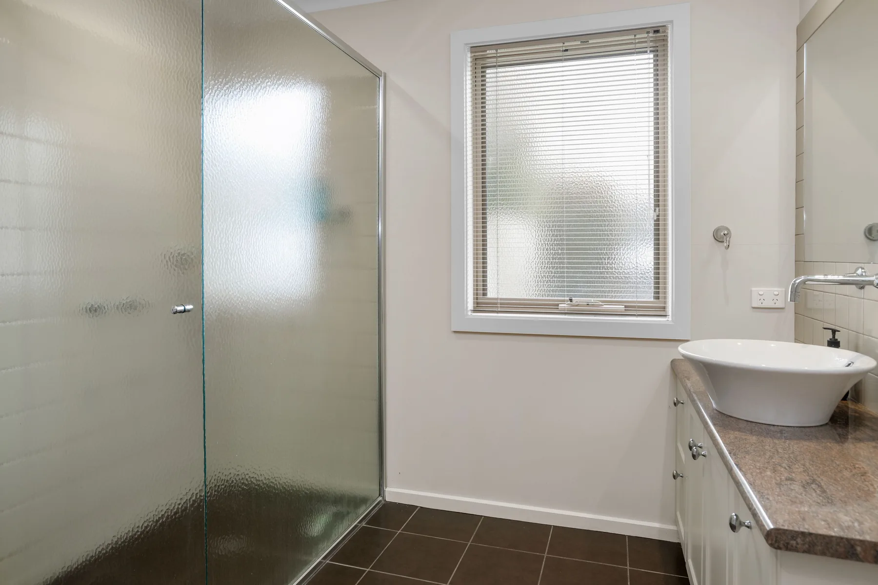 A bathroom with a glass shower, window, and sink.