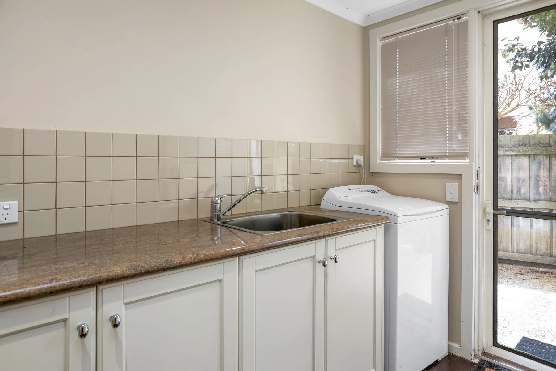 A laundry area with a countertop, sink, and washing machine beside a window.