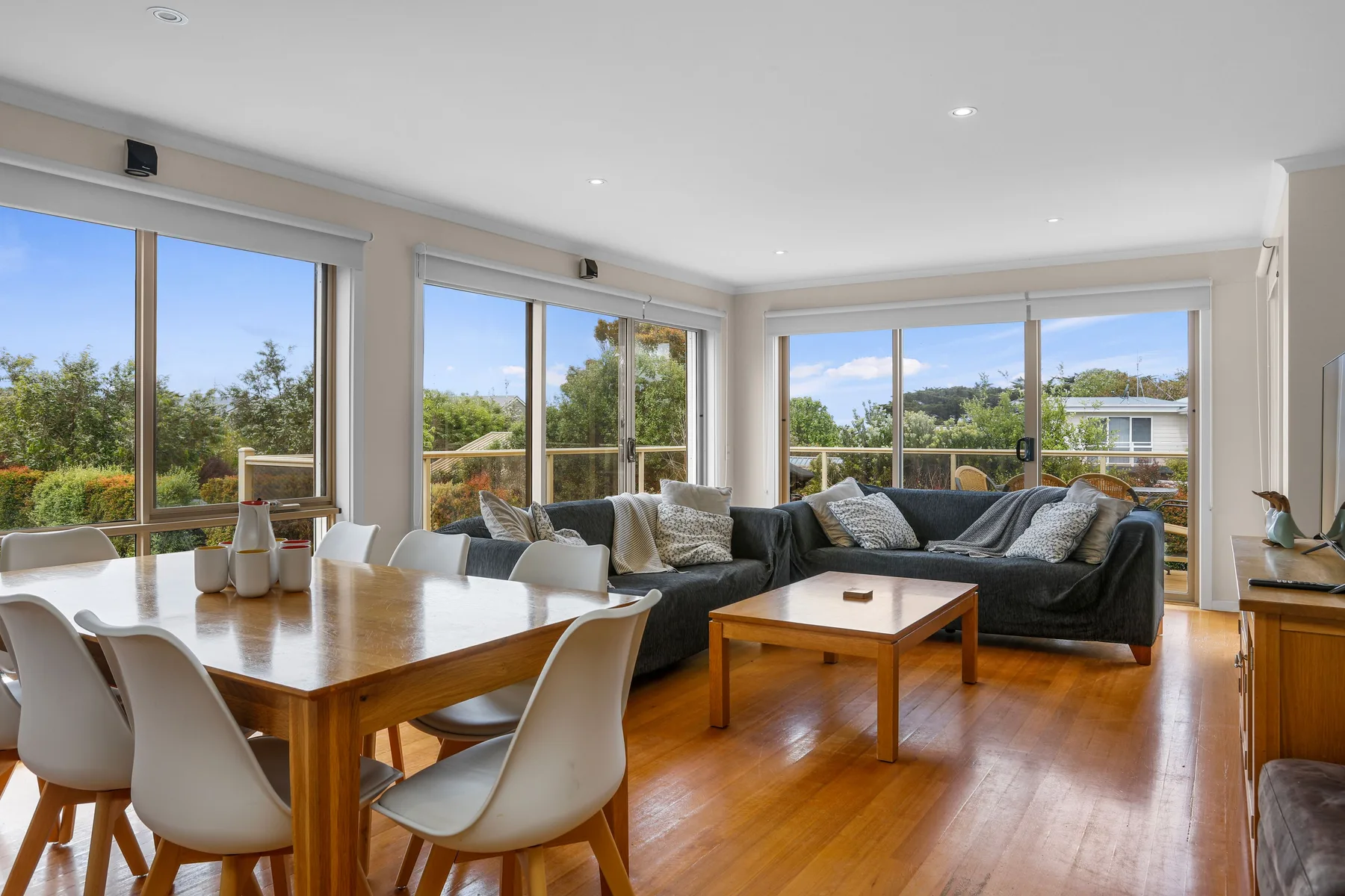 A bright living and dining area with large windows overlooking greenery.