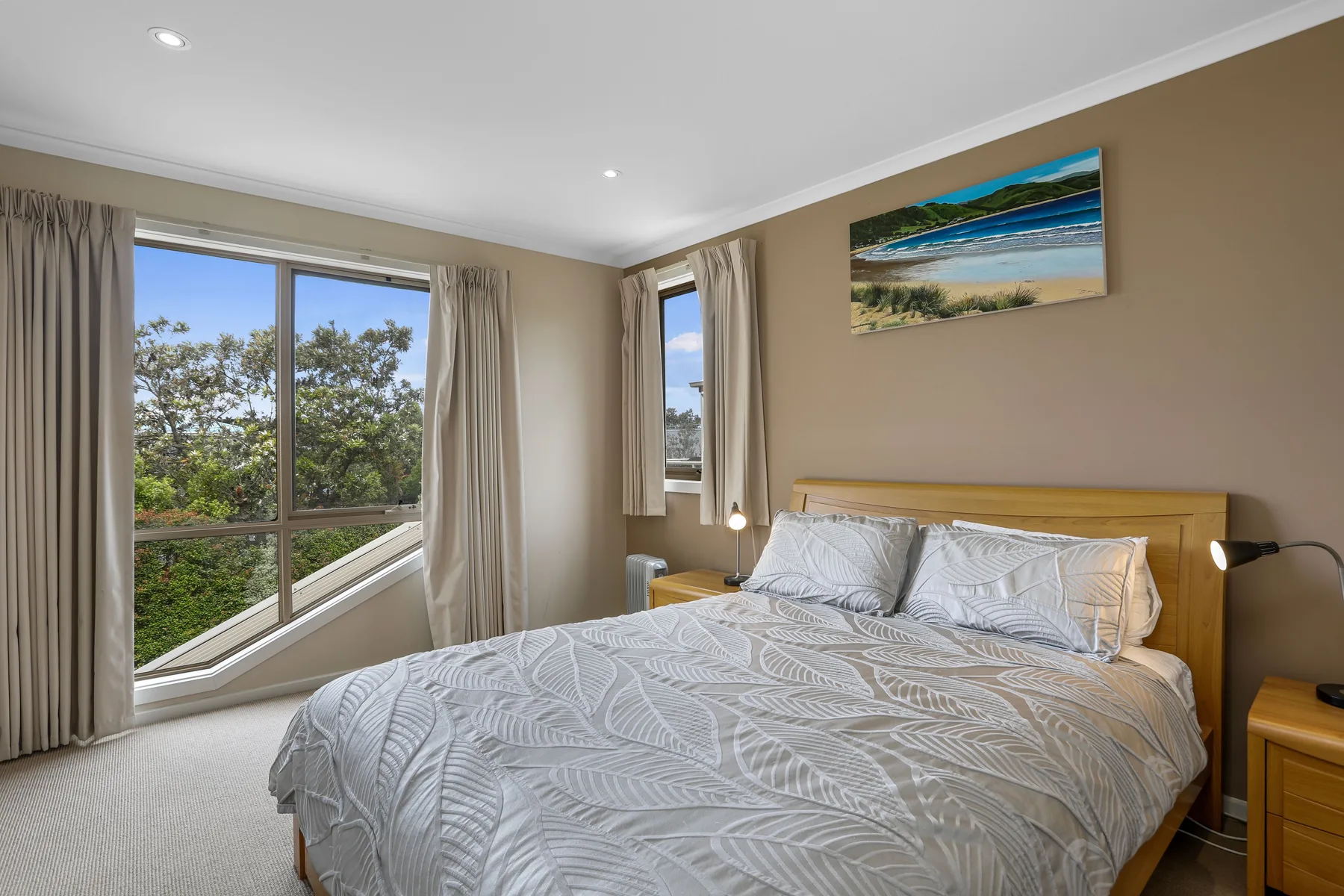A bedroom with a neatly made bed beside large windows.