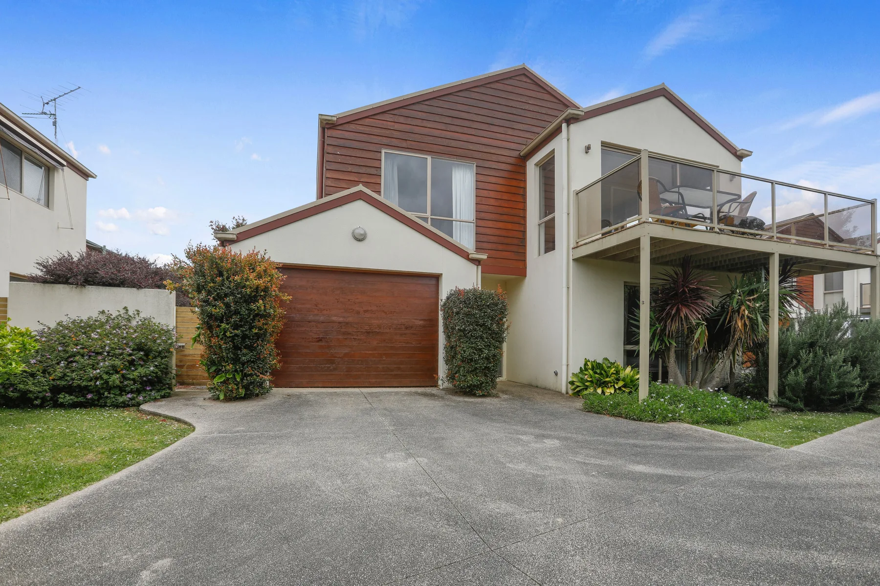 A modern house with a wooden garage door and an upper balcony.