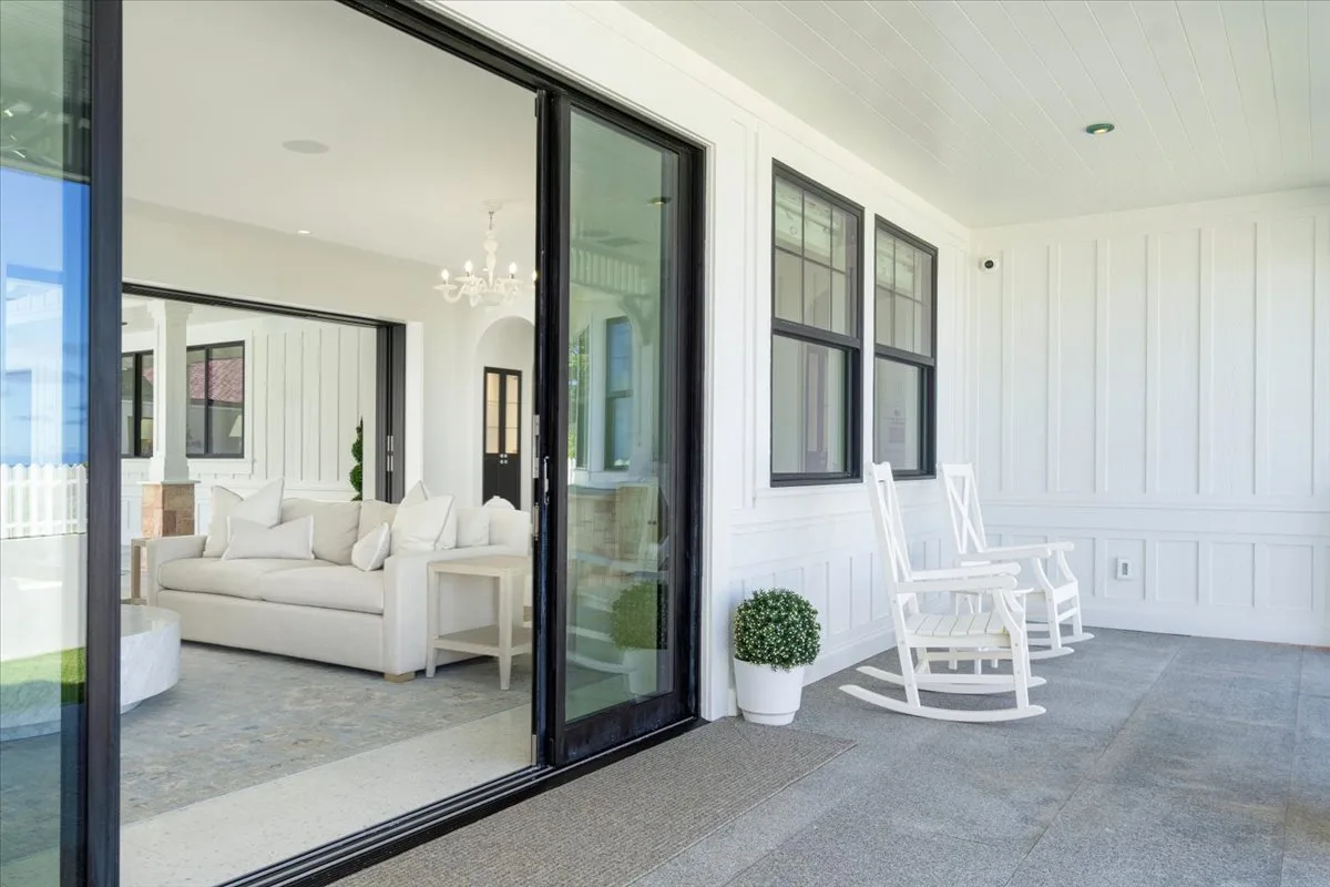 A bright covered porch with rocking chairs beside open sliding glass doors.