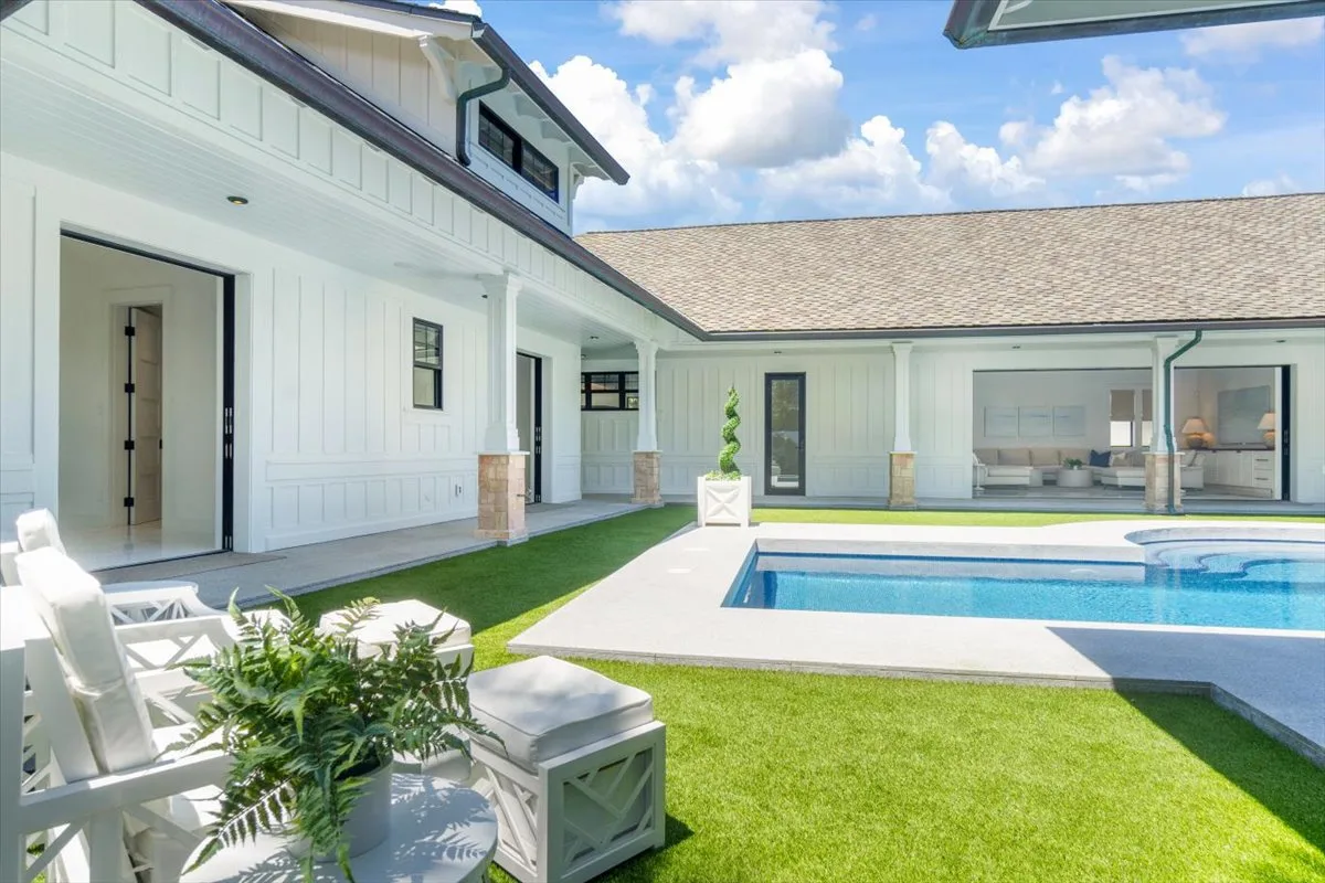 A courtyard pool sits beside a white building, with lawn and patio seating.