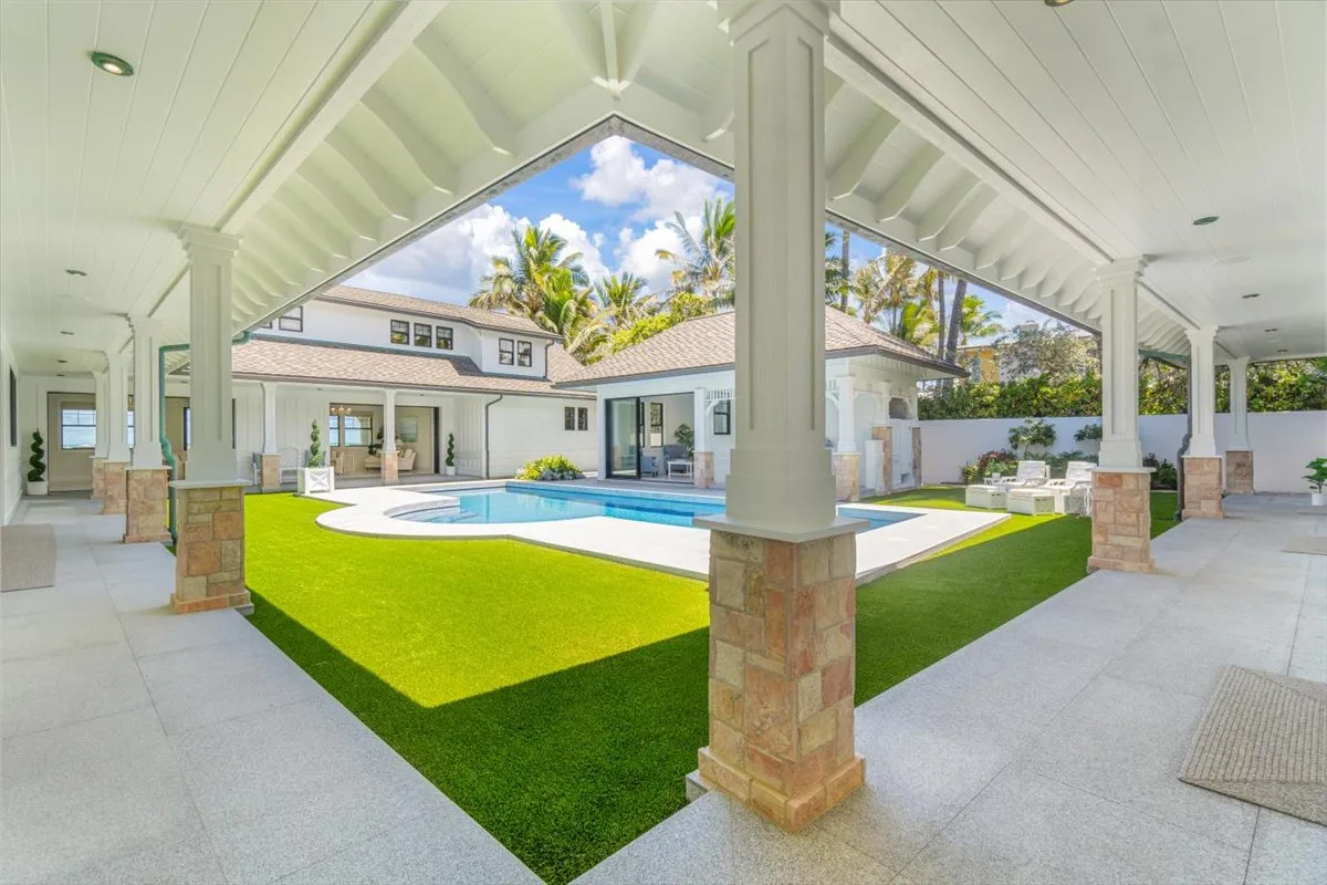 A covered patio overlooks a swimming pool and a bright green lawn.