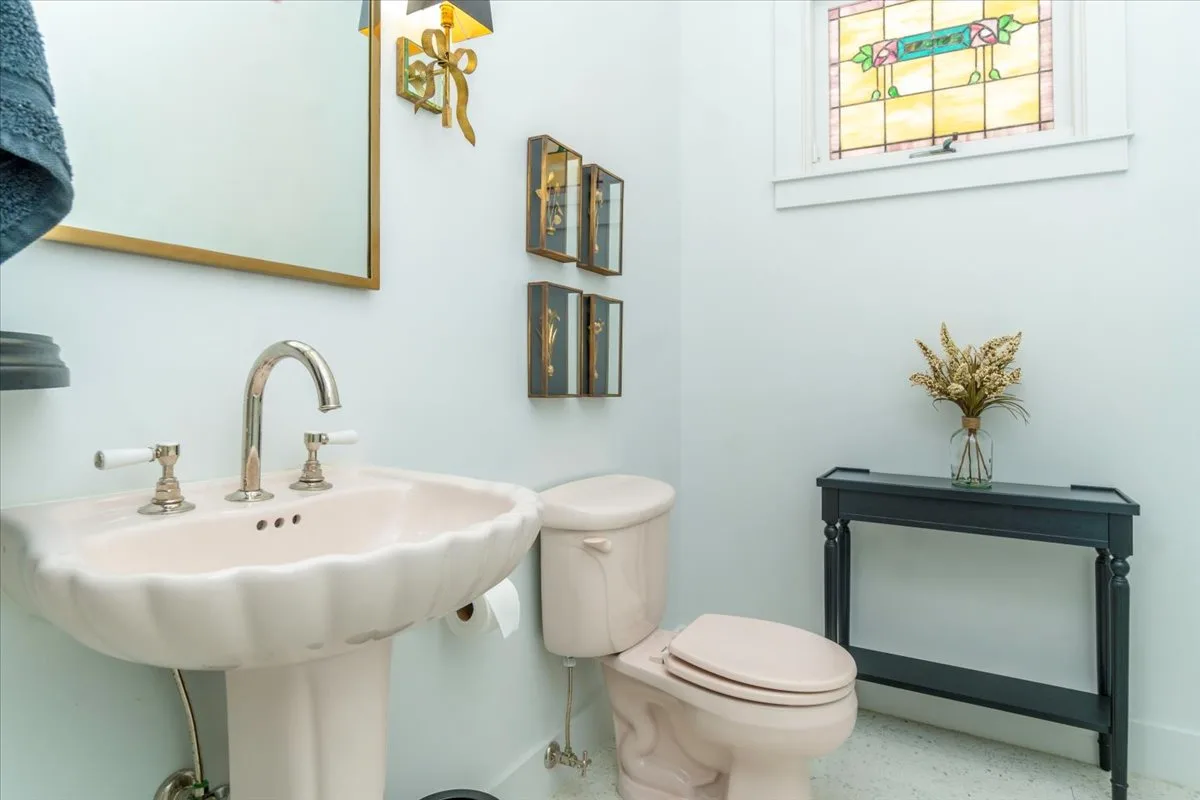 A bathroom with a pedestal sink and toilet beside a narrow console table.