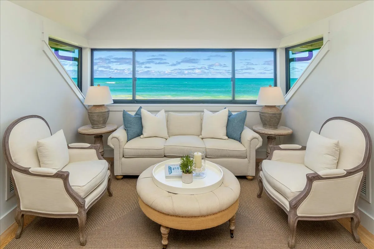 A bright living room with a sofa and chairs facing a large ocean-view window.