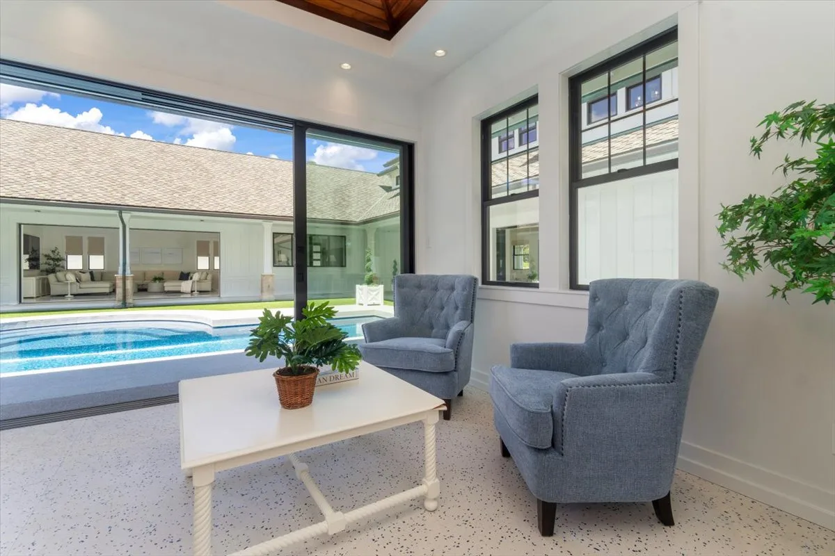 A bright sitting area with two upholstered seats and a coffee table beside large windows.