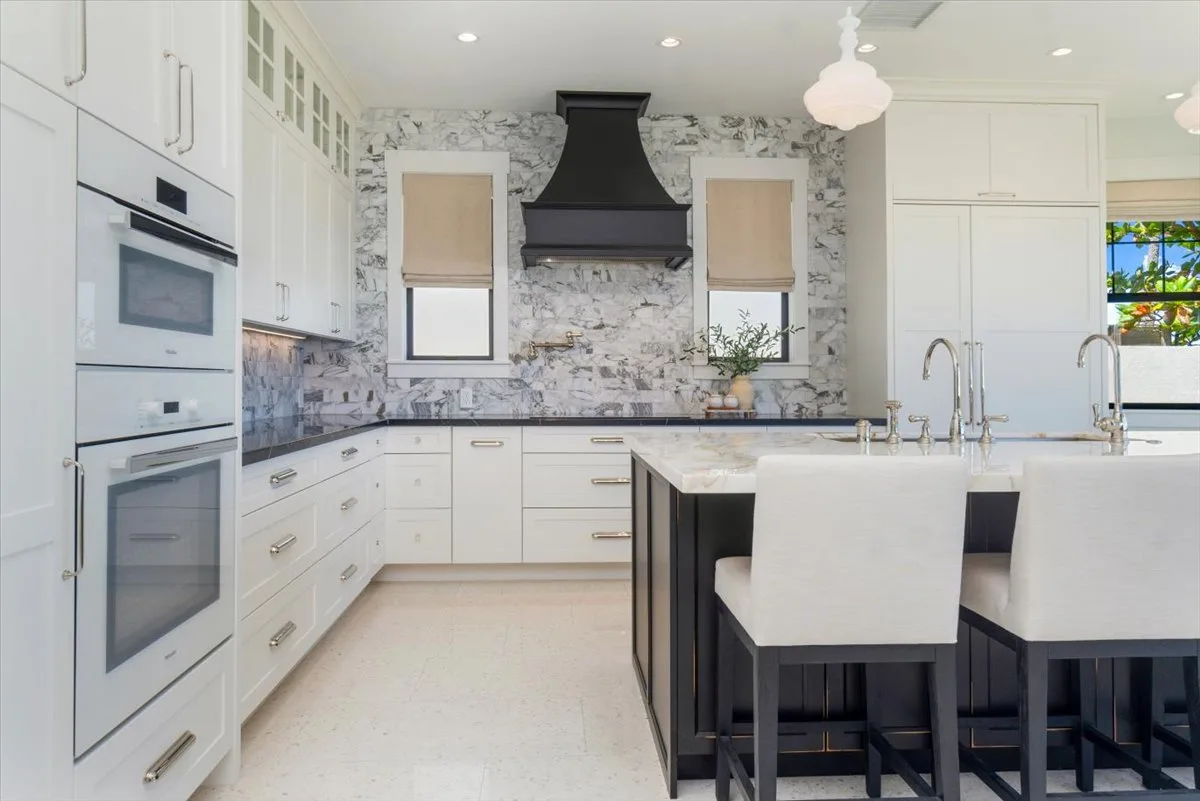 Una cocina luminosa con gabinetes blancos, una isla oscura y un salpicadero estampado.