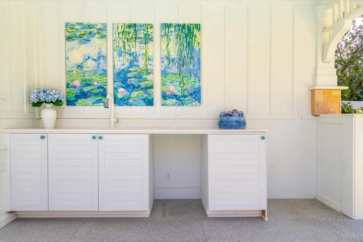 A bright white room with built-in cabinets beneath three colorful paintings.