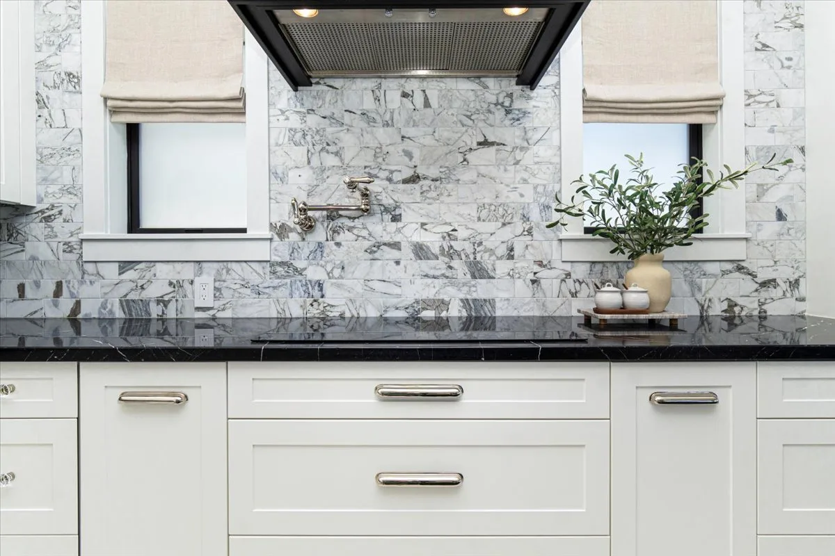 A marble-backed kitchen counter sits beneath a large range hood.