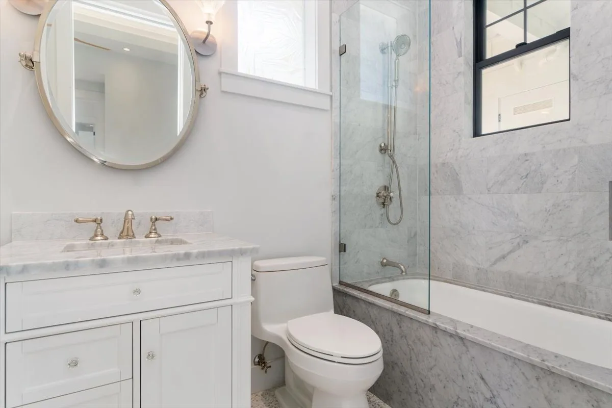 A bright bathroom with a white vanity, toilet, and glass shower.