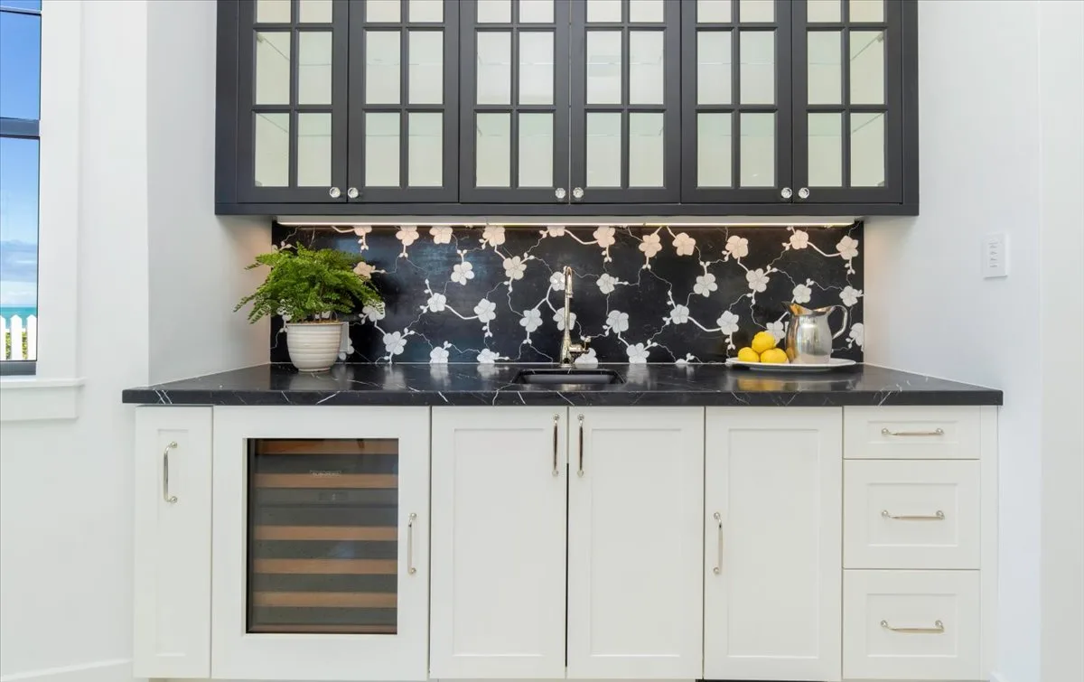 A bright kitchen has white cabinets, dark upper cupboards, and a patterned backsplash.