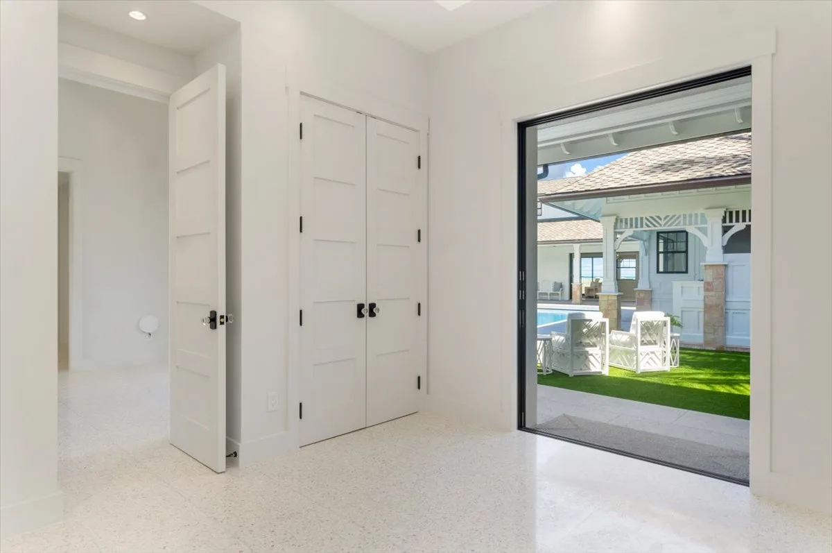 A bright interior room opens onto a patio with seating and a lawn.