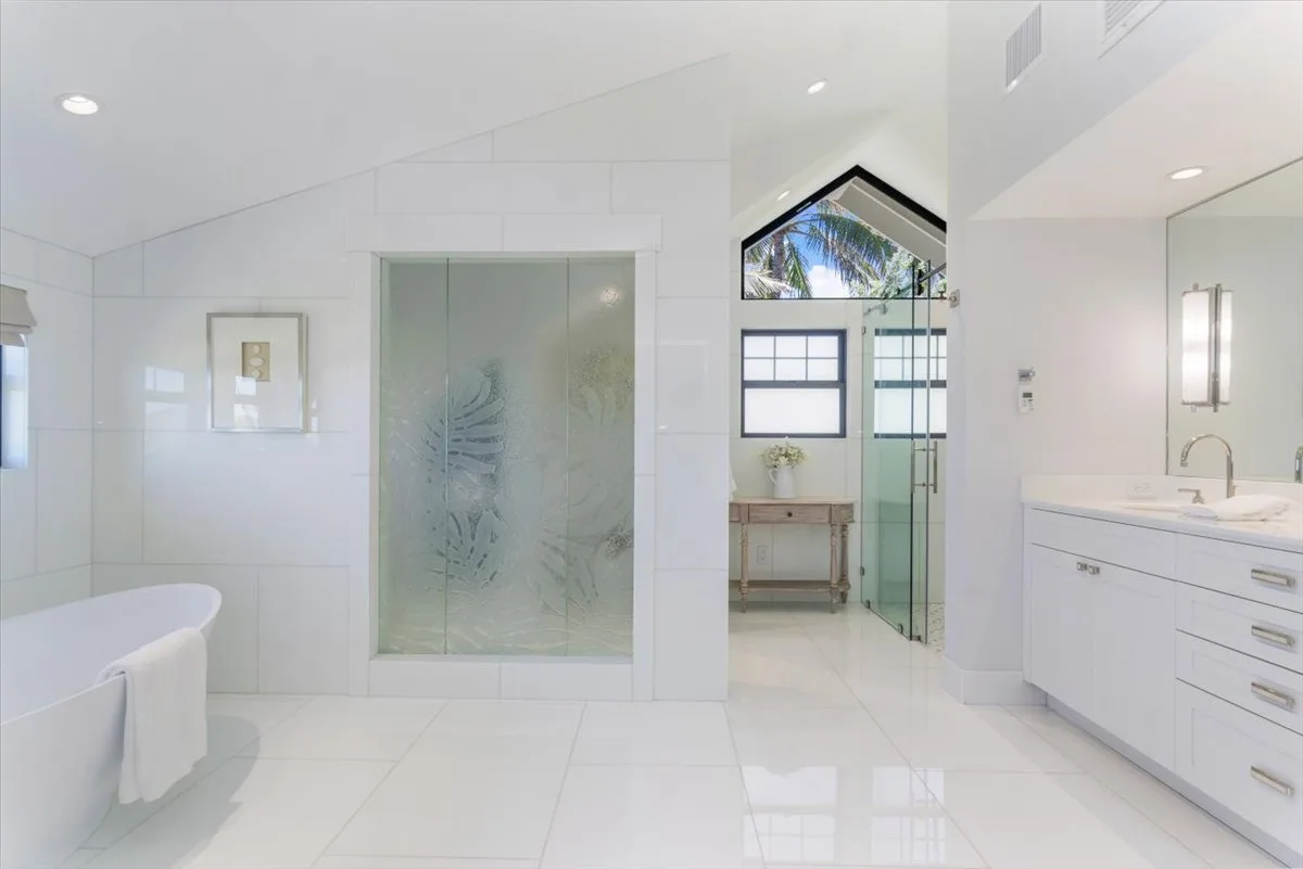 A bright bathroom with a frosted glass shower and a long vanity.