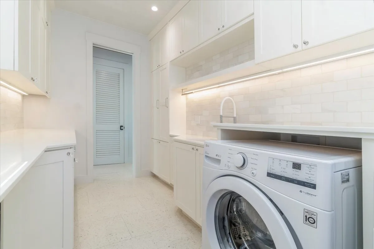 A bright laundry room with a front-loading washing machine and built-in cabinets.