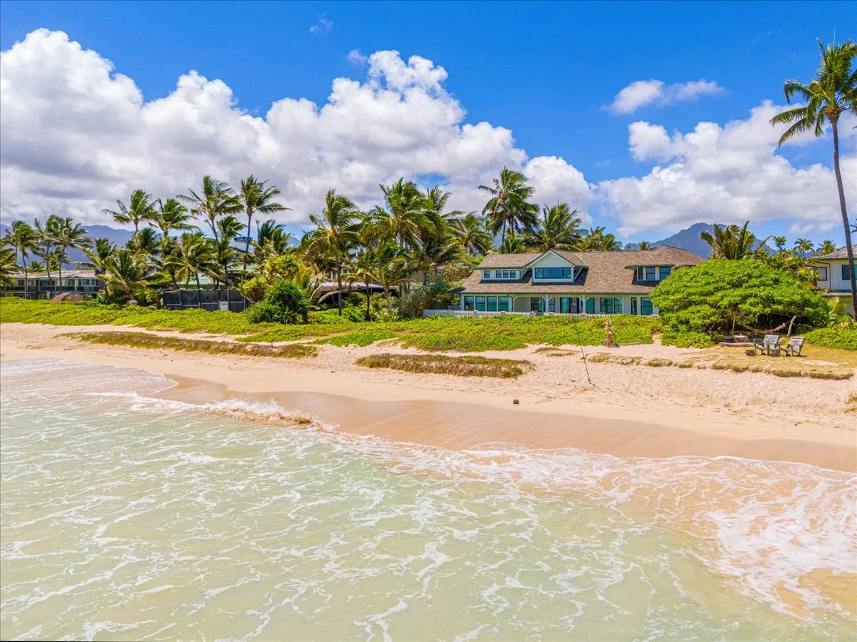 A tropical beach with palm trees and a house along the shore.