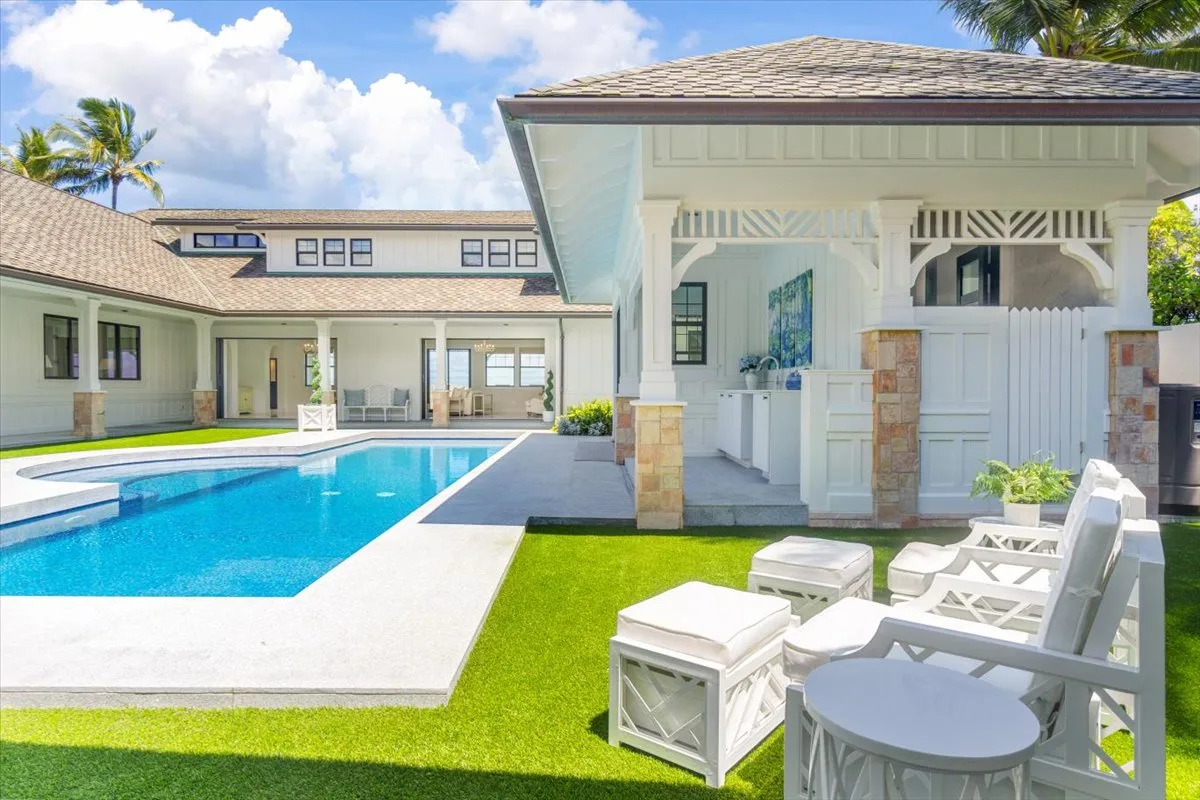 Un patio luminoso con piscina, asientos blancos y una zona cubierta.