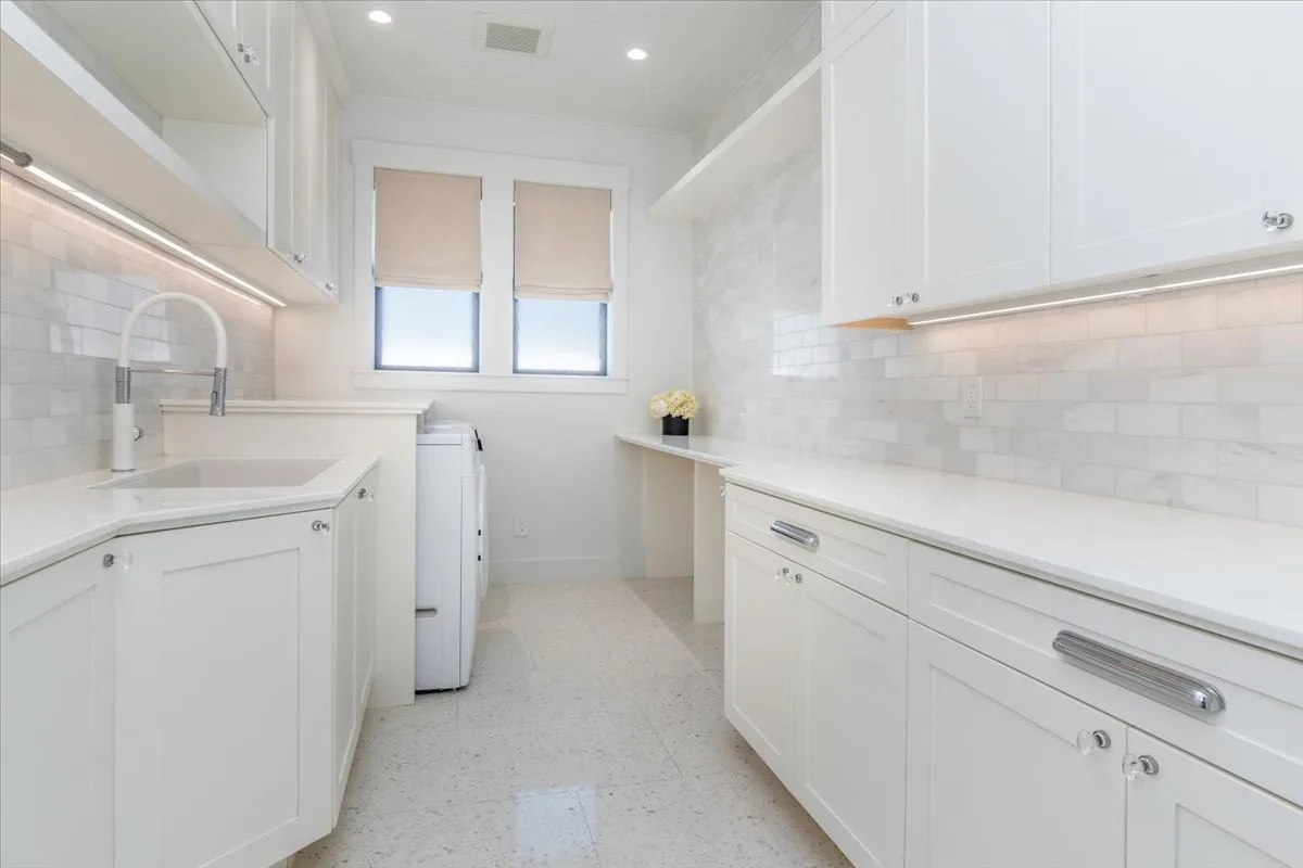 A bright white kitchen with counters, cabinets, and two windows.