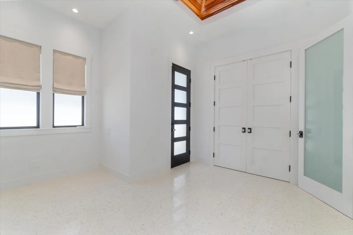 A bright white room with windows, double doors, and a dark-framed glass door.