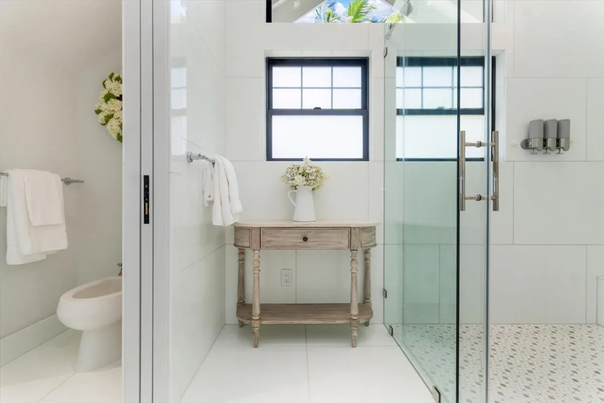 A bright bathroom with a wooden vanity beneath a window and a glass shower.