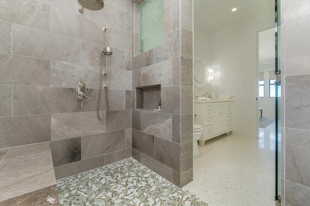 A tiled bathroom with a walk-in shower and a vanity visible beyond.