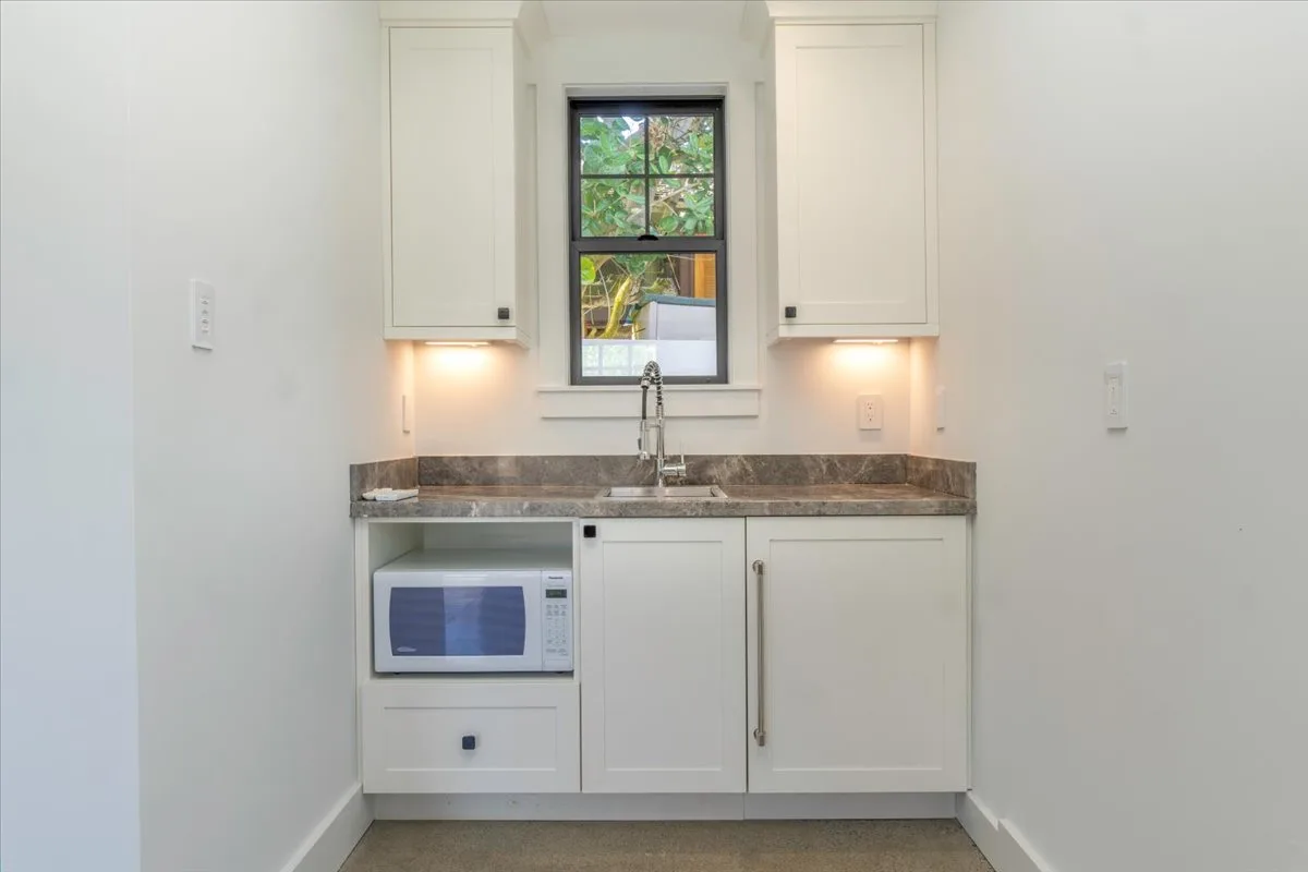 A compact kitchen with a sink beneath a window and white cabinets.